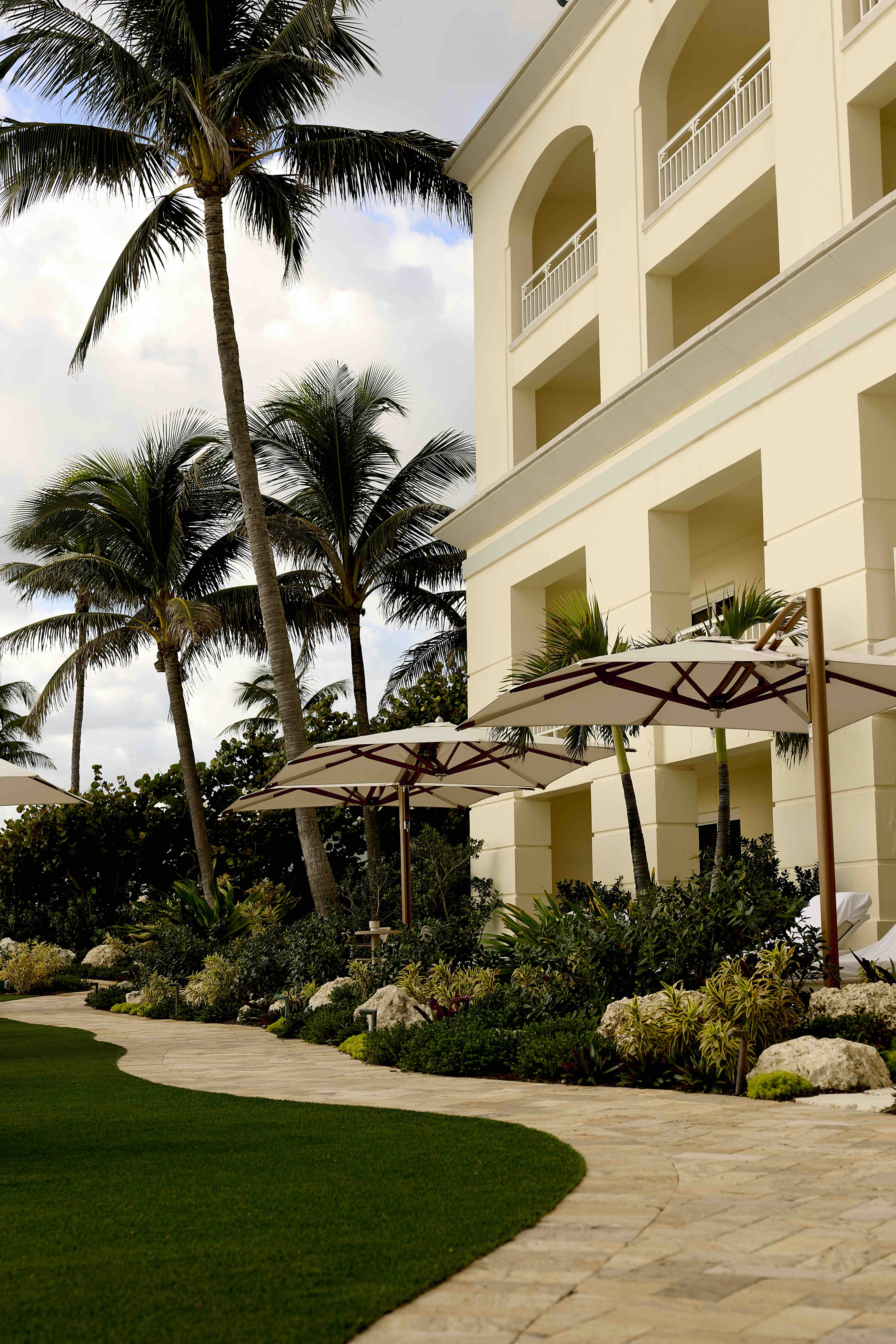 Tropical resort building with palm trees, landscaped garden, and shaded lounge umbrellas