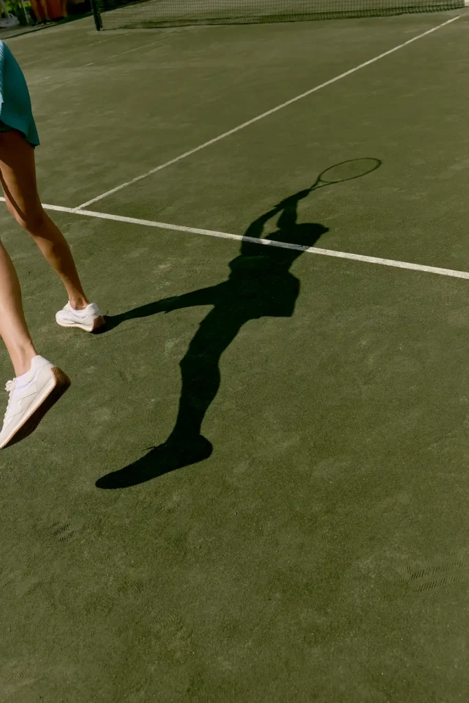 Tennis player’s shadow swinging racket on sunlit outdoor court