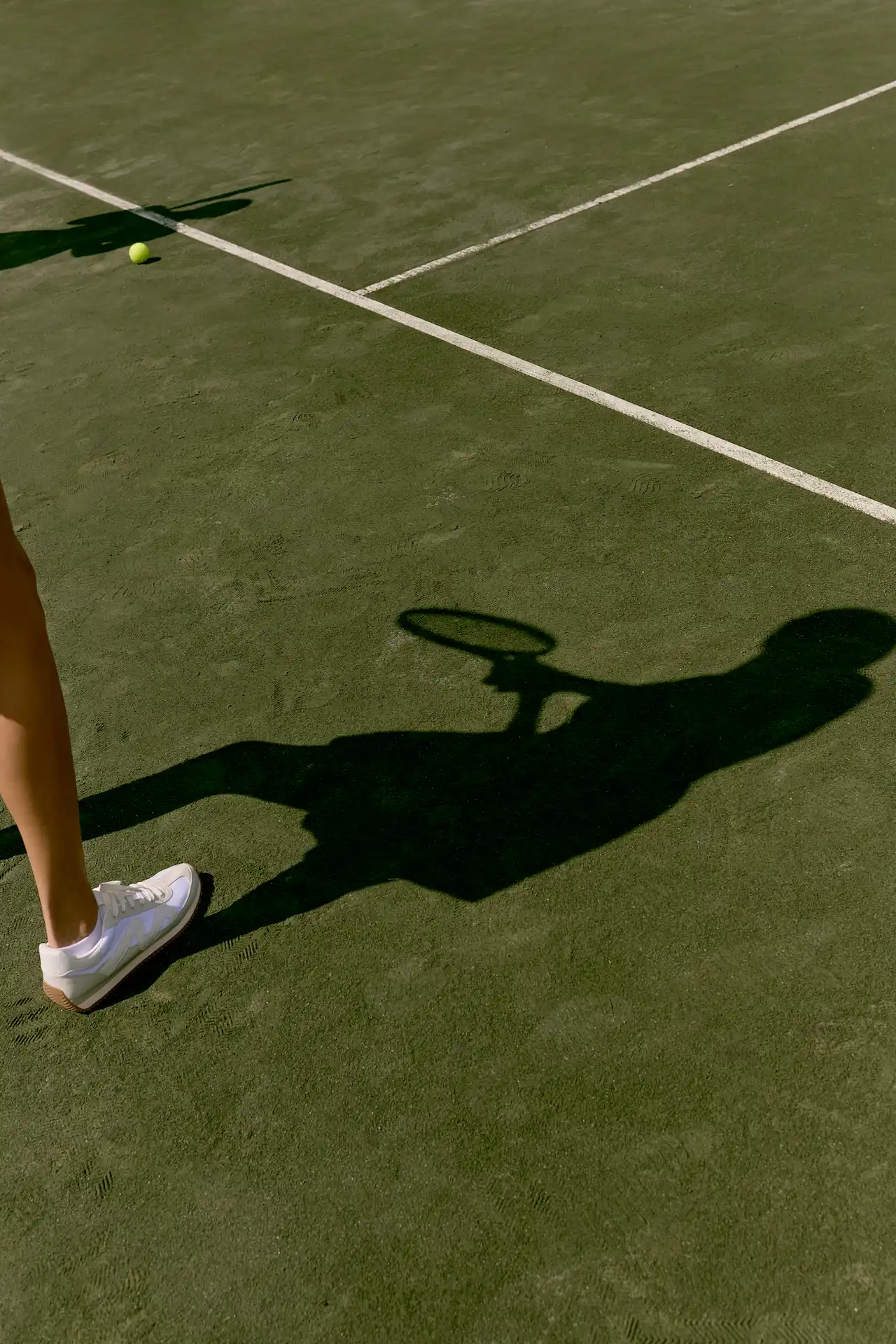 Shadow of tennis player with racket on court near ball and boundary line