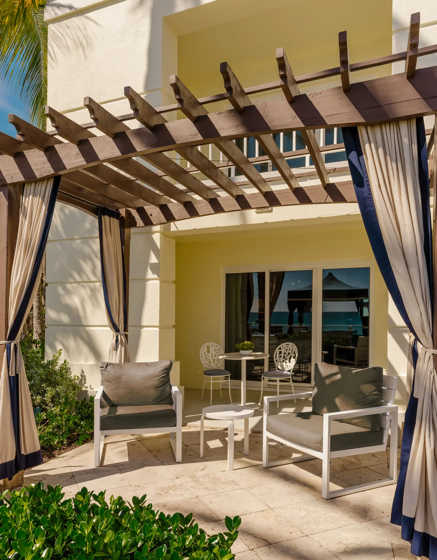 Sunny patio with cushioned chairs under pergola outside seaside villa suite