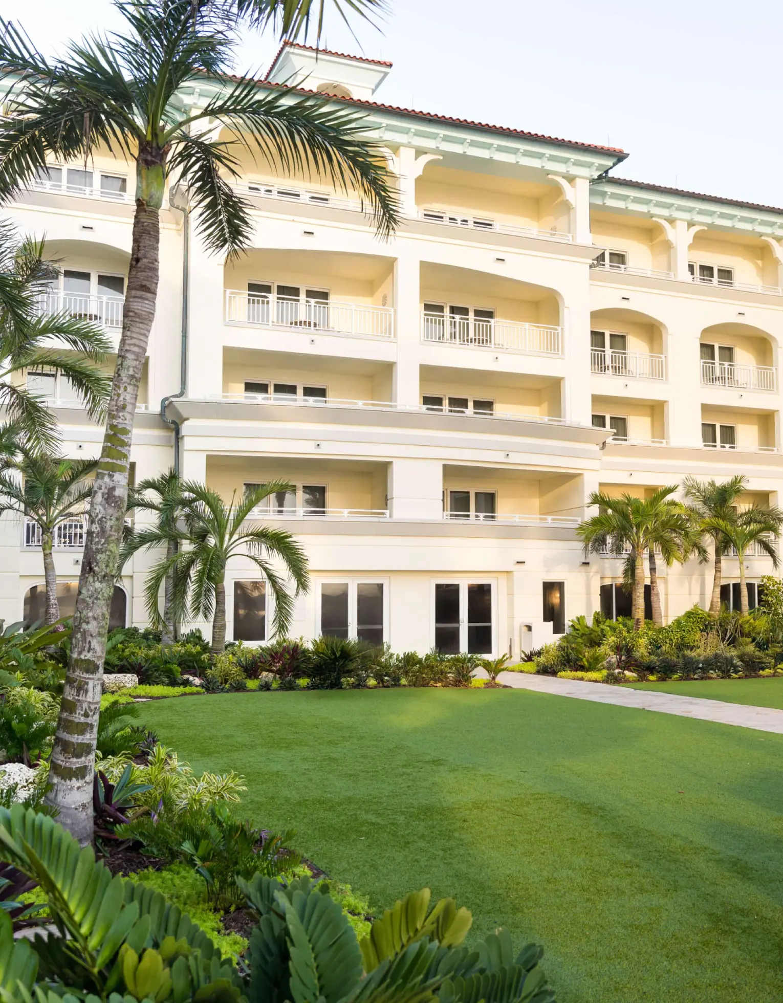 Luxury beachfront resort courtyard with palm trees, manicured lawn, and multi-story balconies in warm sunlight