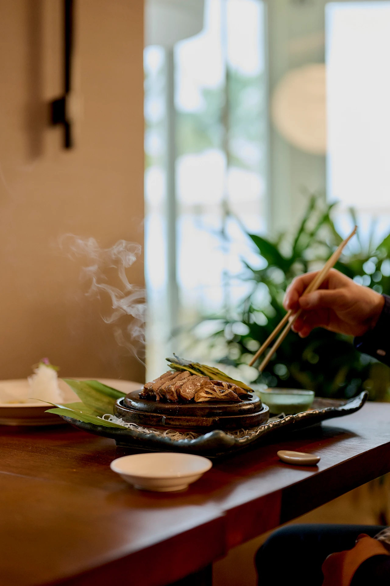 Steaming grilled dish being served with chopsticks at nobu, presented on a vibrant, elegant platter