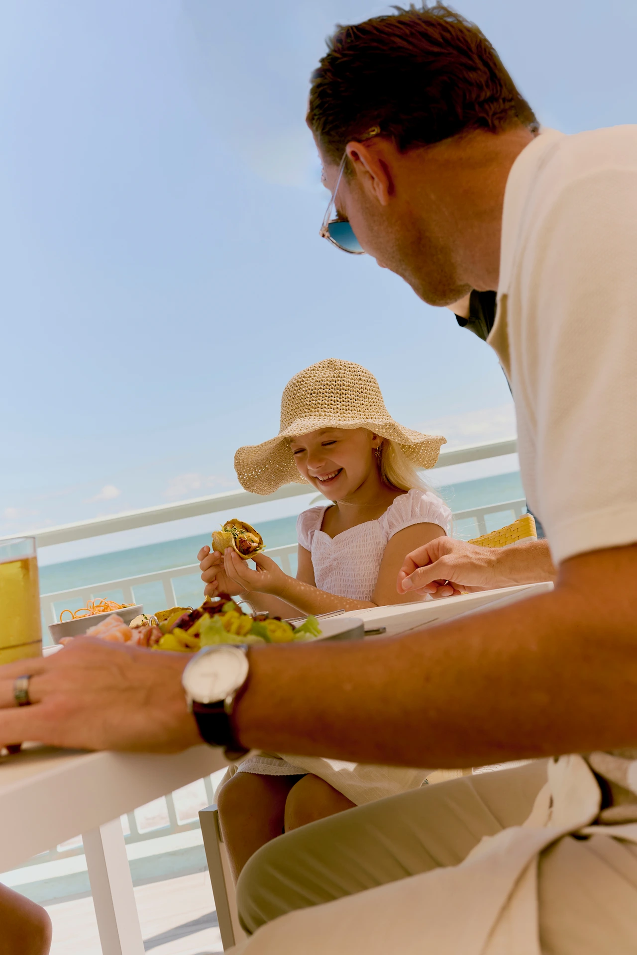 Father and daughter enjoying lunch on seaside balcony under sunny sky