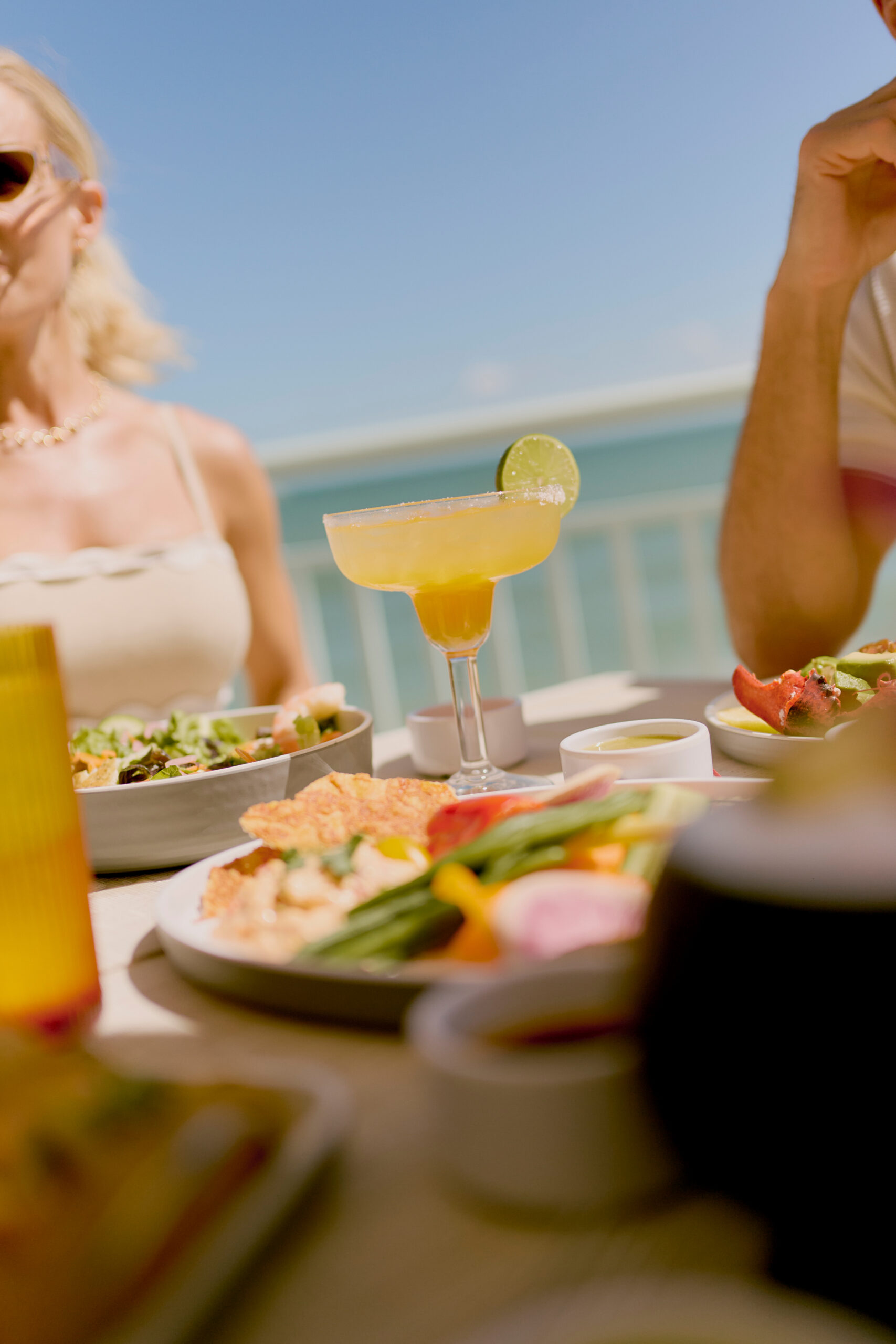 Outdoor lunch with margarita, salads, and seafood on a sunny beachfront patio