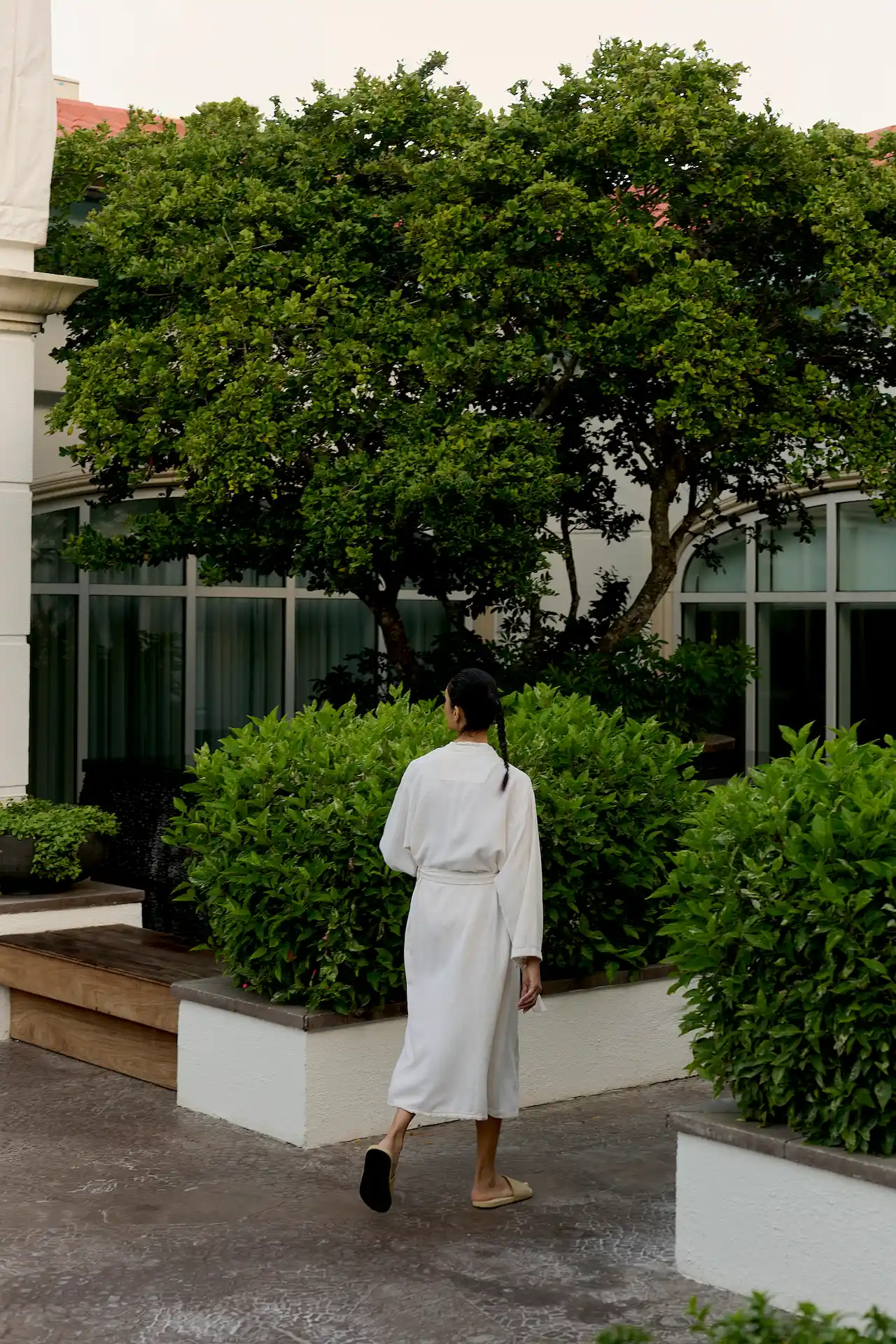 Woman in white robe walking through lush courtyard garden at resort