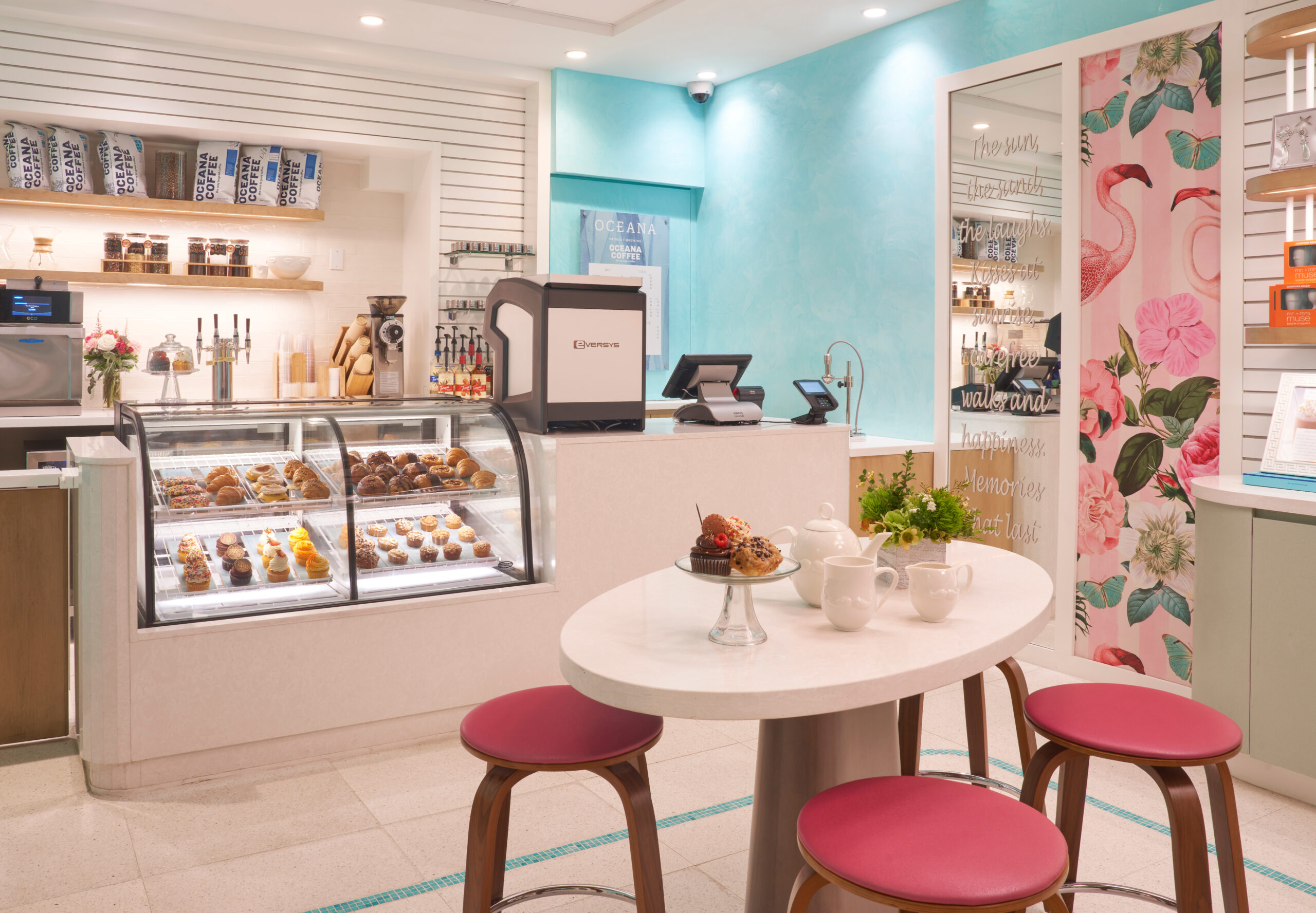Bright café interior with pastry display case, coffee station, and round table with pink stools