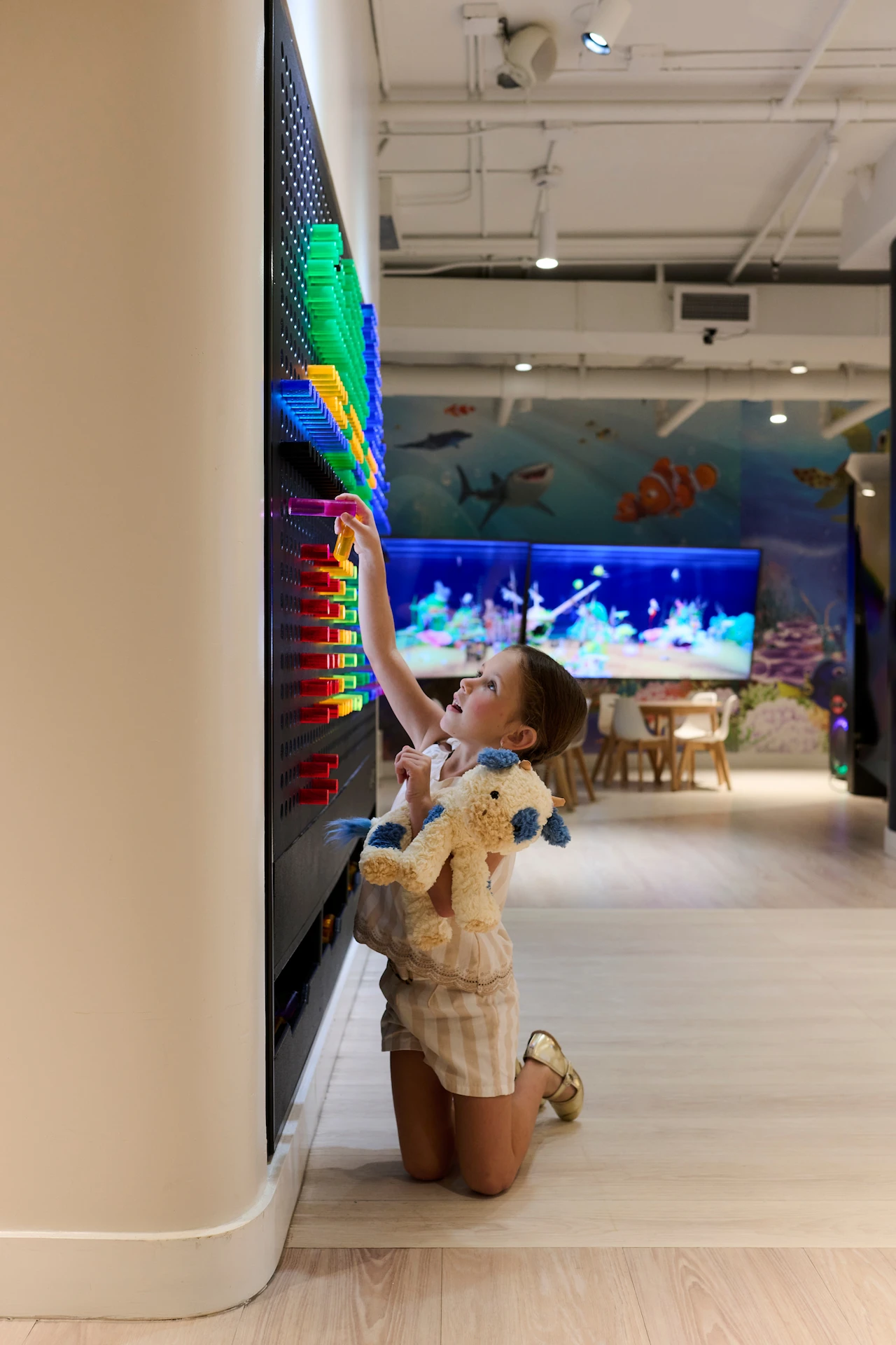 Child placing a bright peg on a colorful wall in a playful marine‑themed area filled with vibrant underwater decor