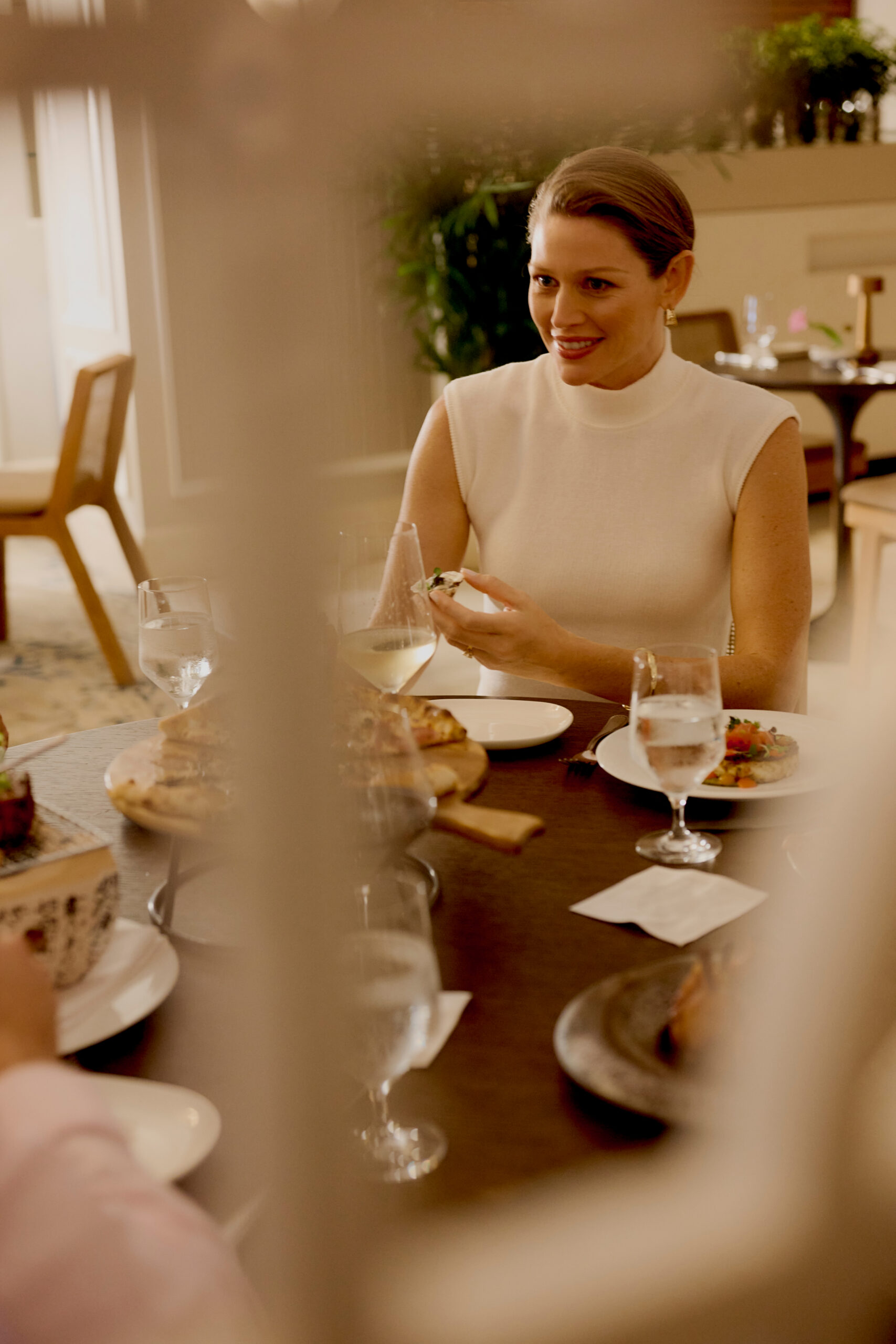 Woman in white top enjoying dinner and wine at warmly lit restaurant table