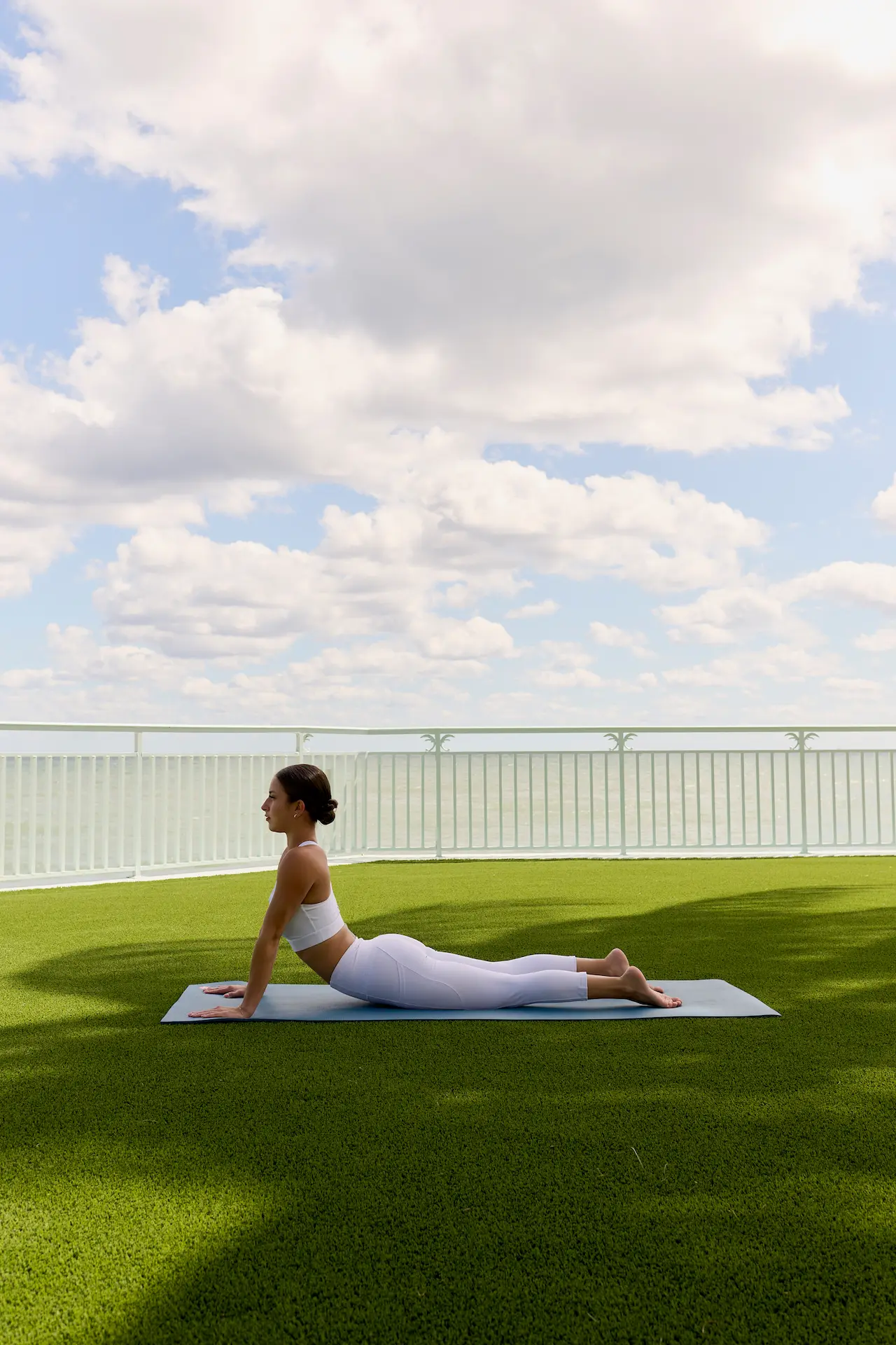 Woman practicing yoga on mat overlooking ocean under bright cloudy sky