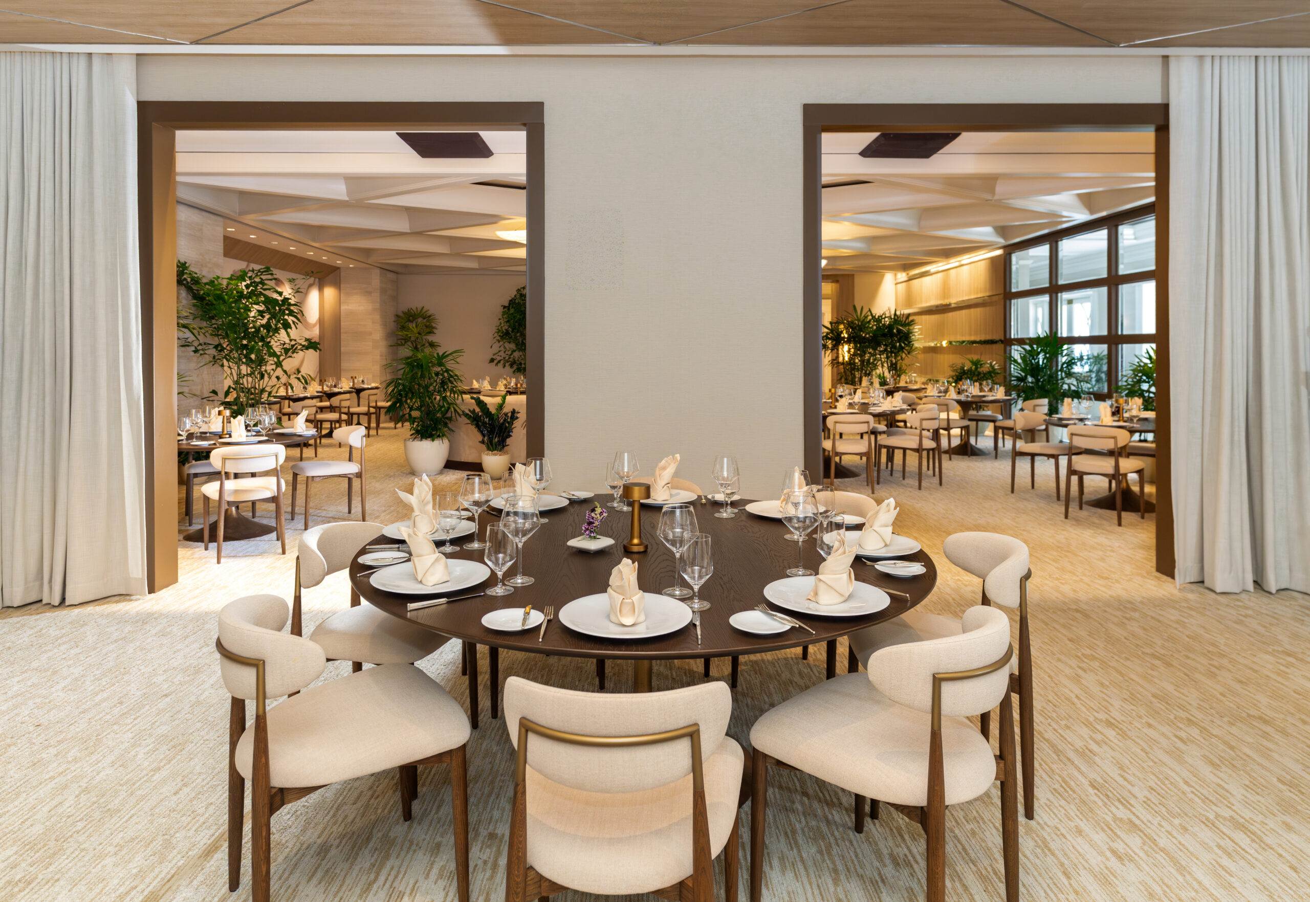 Elegant private dining room with round table set for eight, soft lighting, neutral decor, and indoor plants