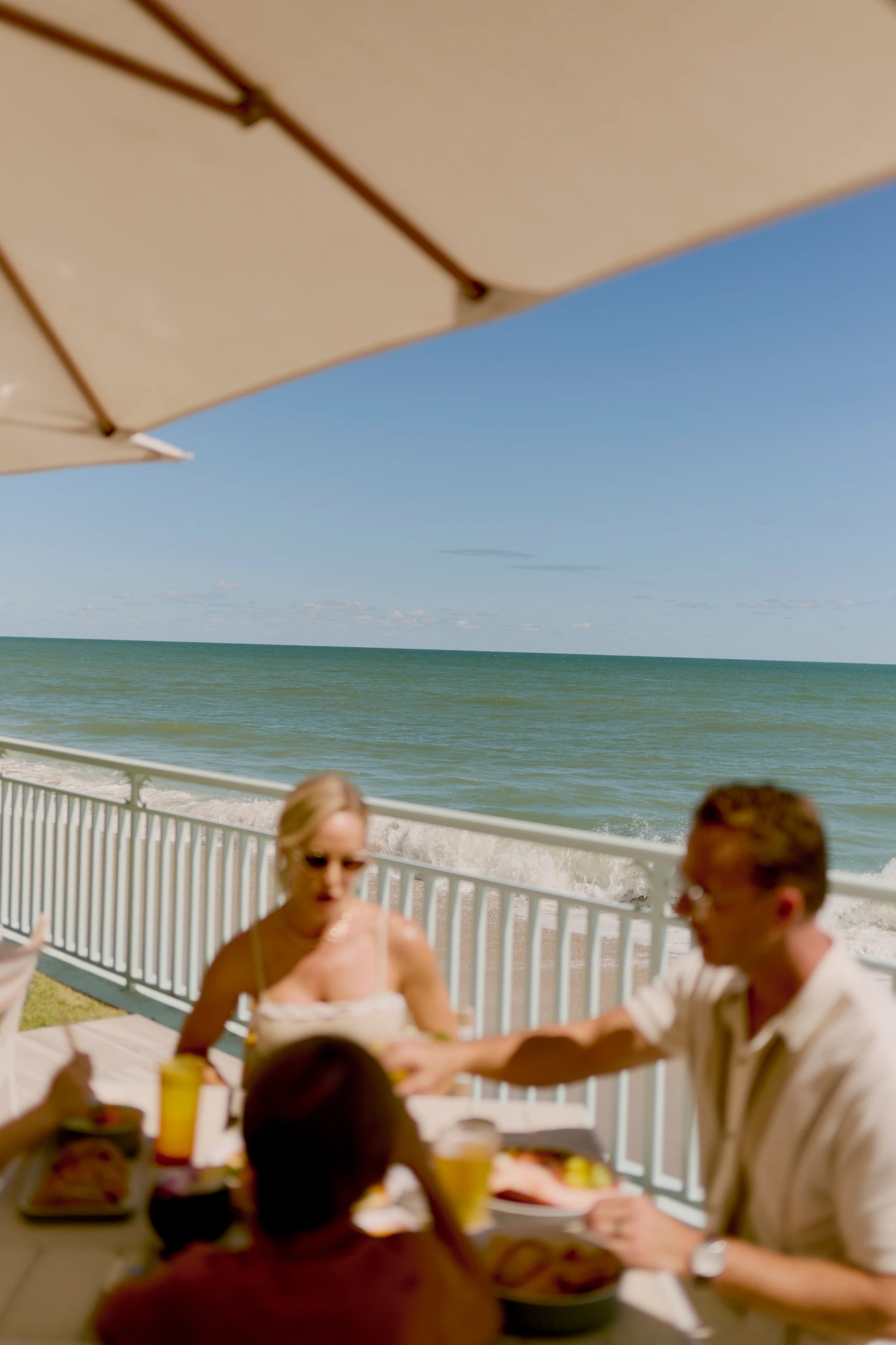 Guests enjoy an oceanfront meal with waves and soft sunlight creating a relaxed coastal atmosphere