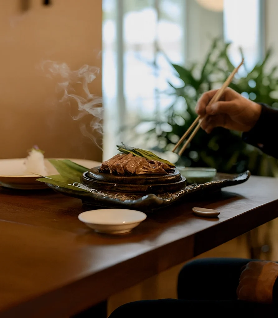 Steaming hot dish being served with chopsticks at a cozy, sunlit table