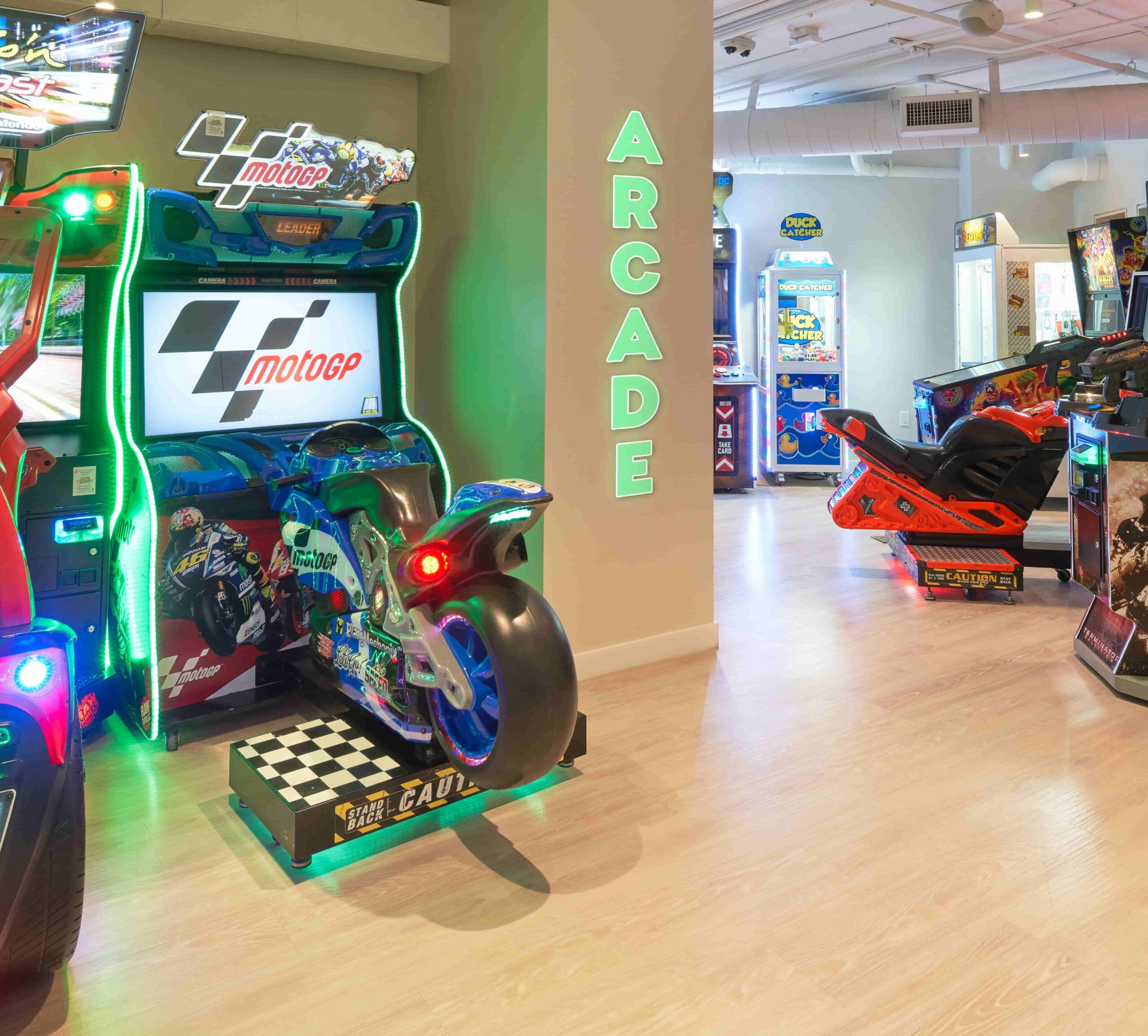 Neon-lit arcade with motorcycle racing and shooting game machines on a wooden floor interior