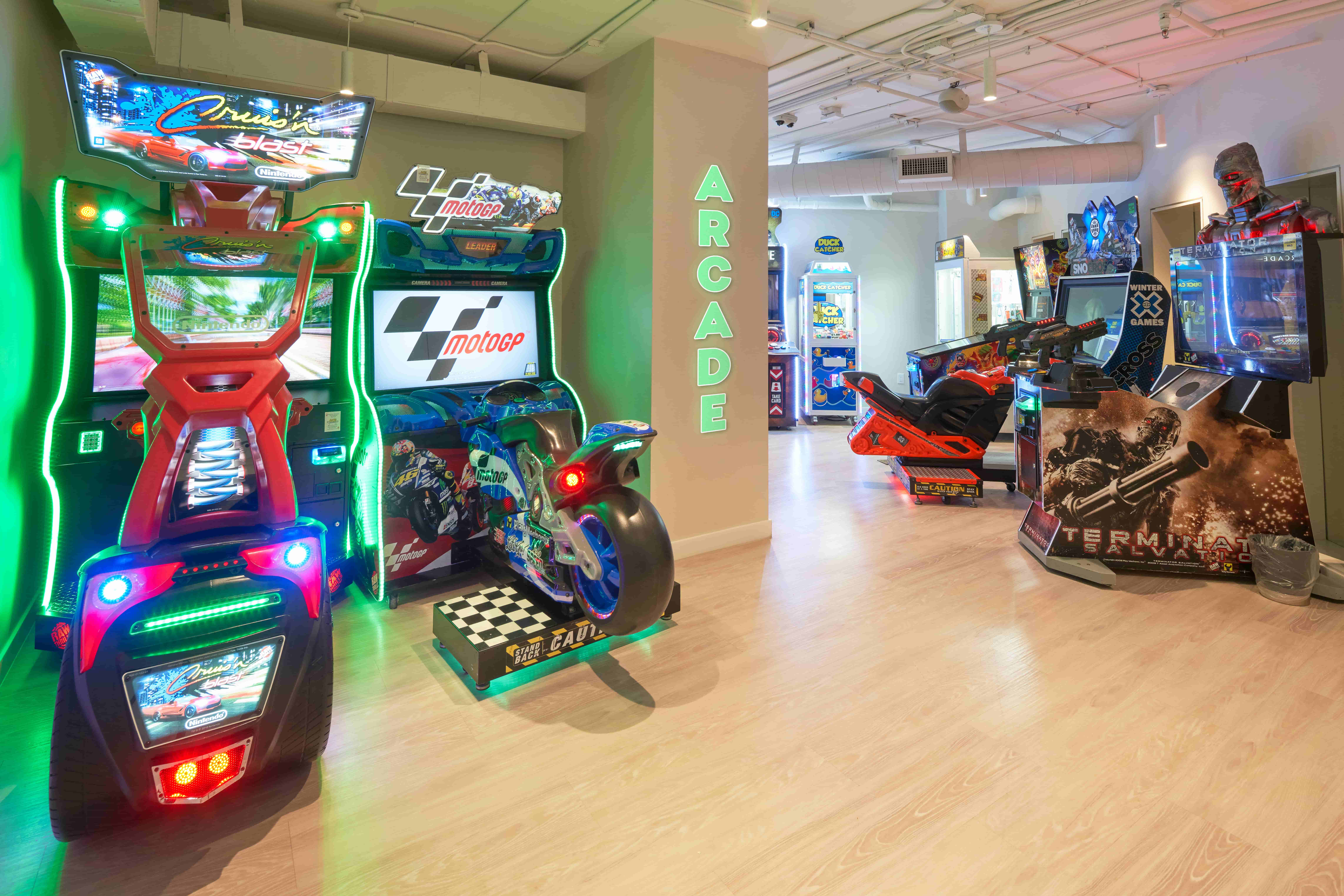 Neon-lit arcade with motorcycle racing and shooting game machines on a wooden floor interior