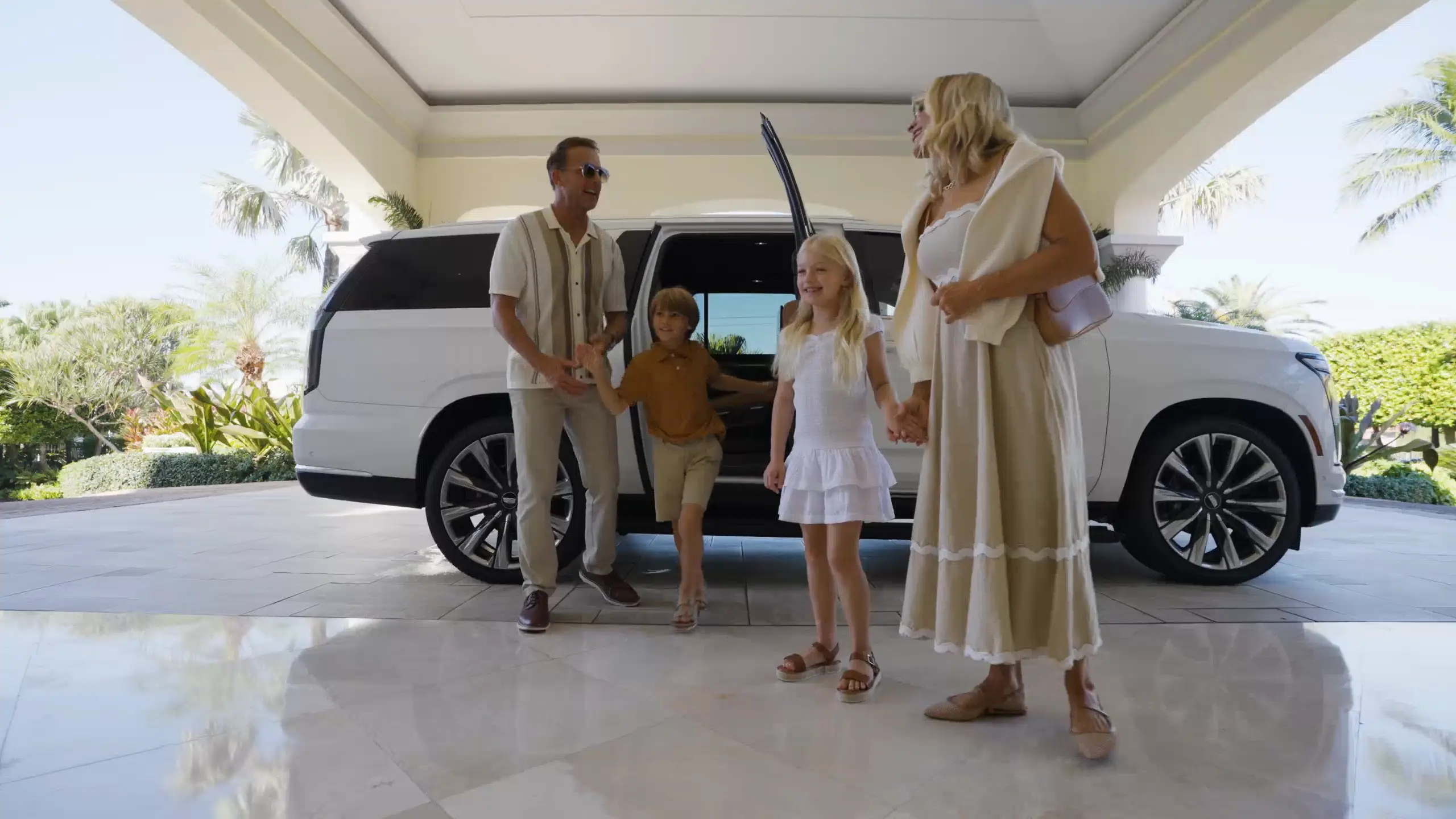 Family stepping out of white suv at sunny resort entrance with palm trees in background