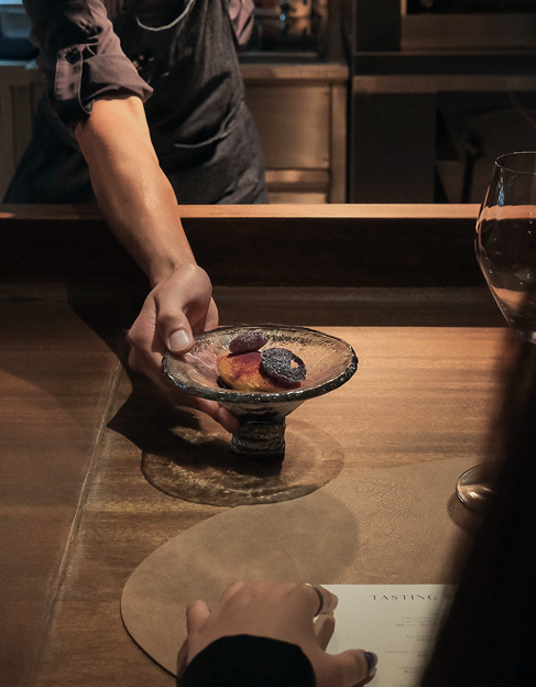 Chef serving plated dessert across wooden counter during intimate dining experience