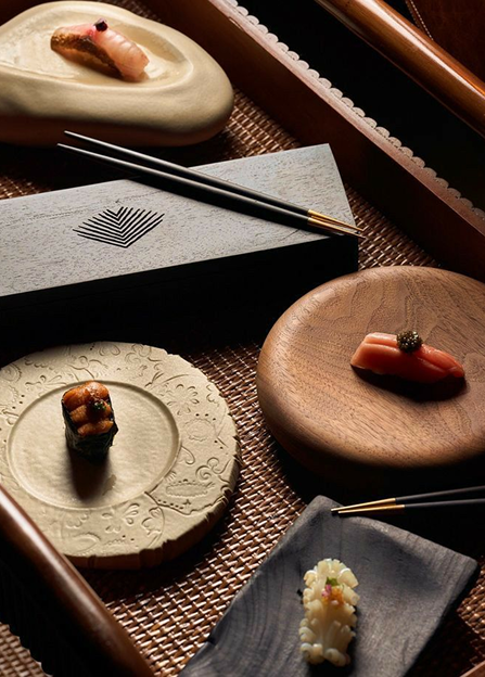 Assorted sushi pieces on ceramic and wooden plates with chopsticks in elegant presentation box