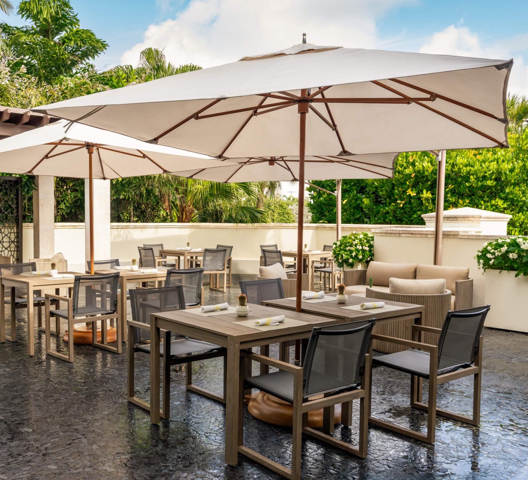 Outdoor patio dining area with umbrellas, wooden tables, and lush tropical greenery