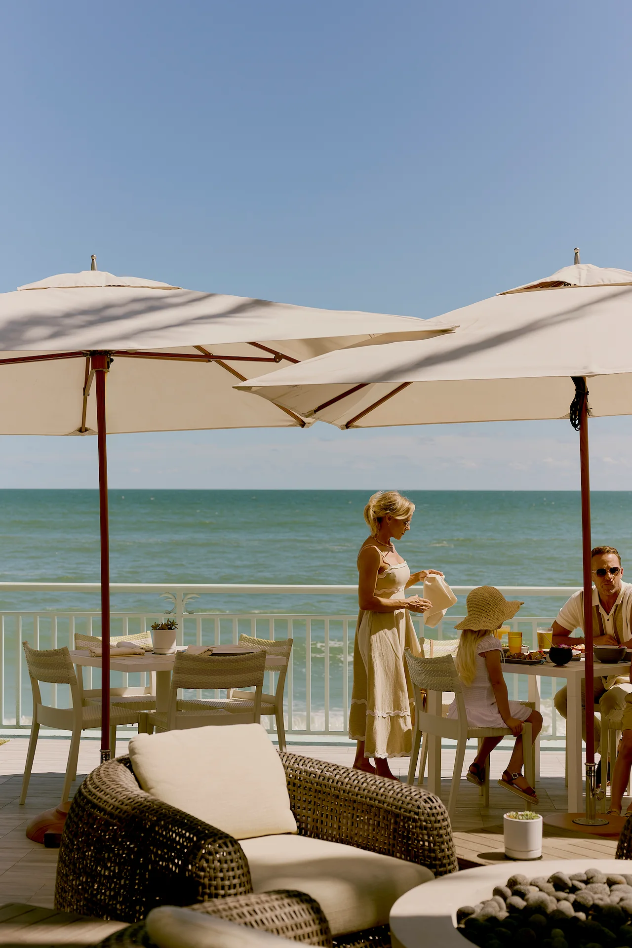 Family dining under umbrellas on oceanfront patio with sea view and outdoor seating