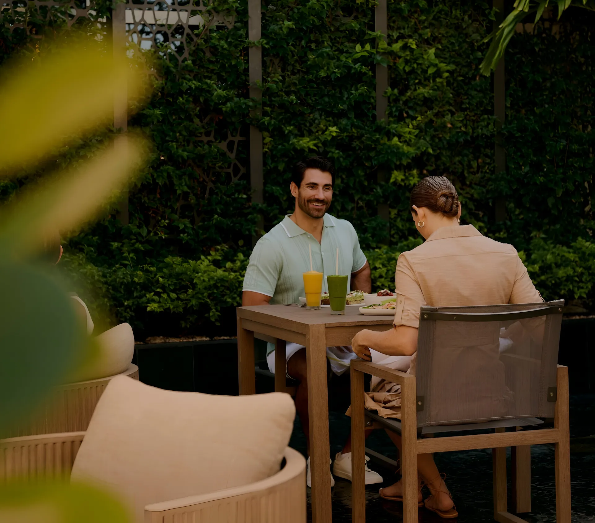 Two people enjoying a relaxed outdoor meal at a wooden table surrounded by lush greenery