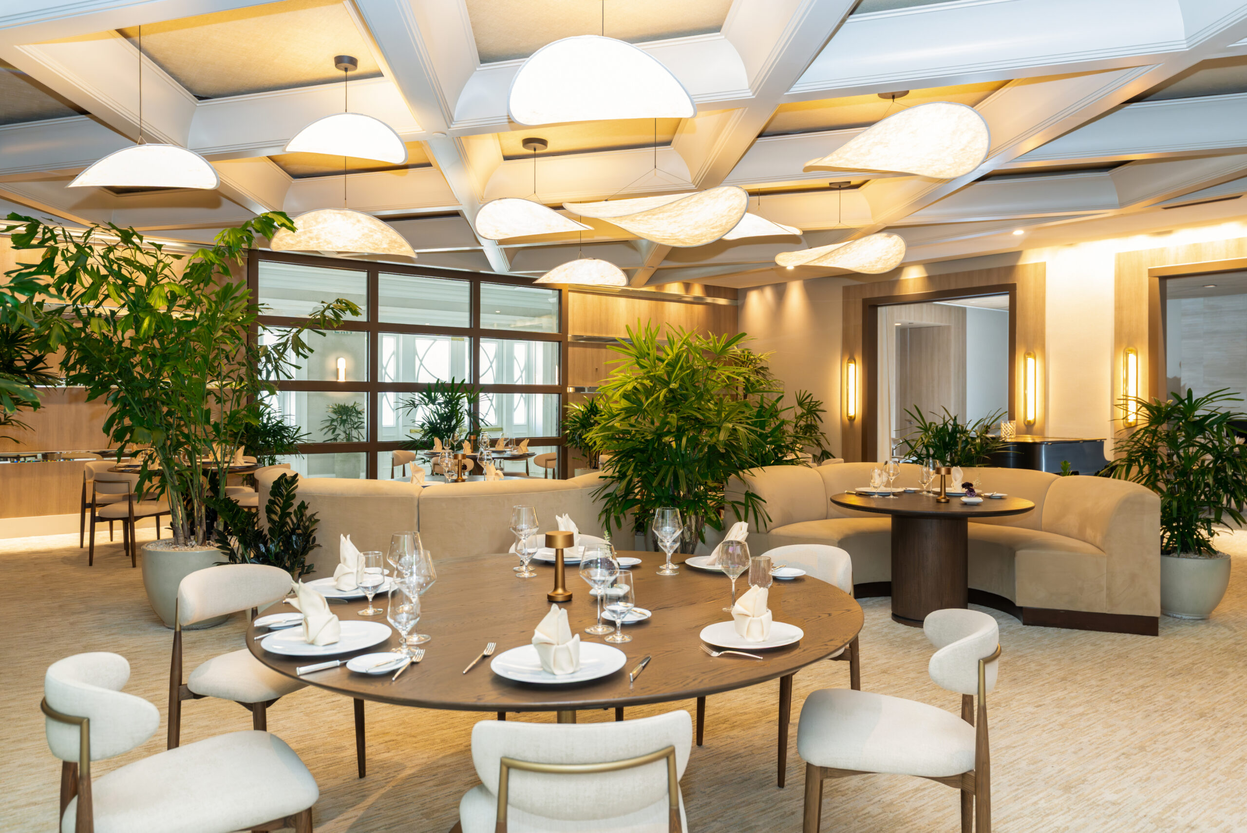 Elegant modern restaurant interior with round tables, plush seating, warm lighting, and lush indoor plants
