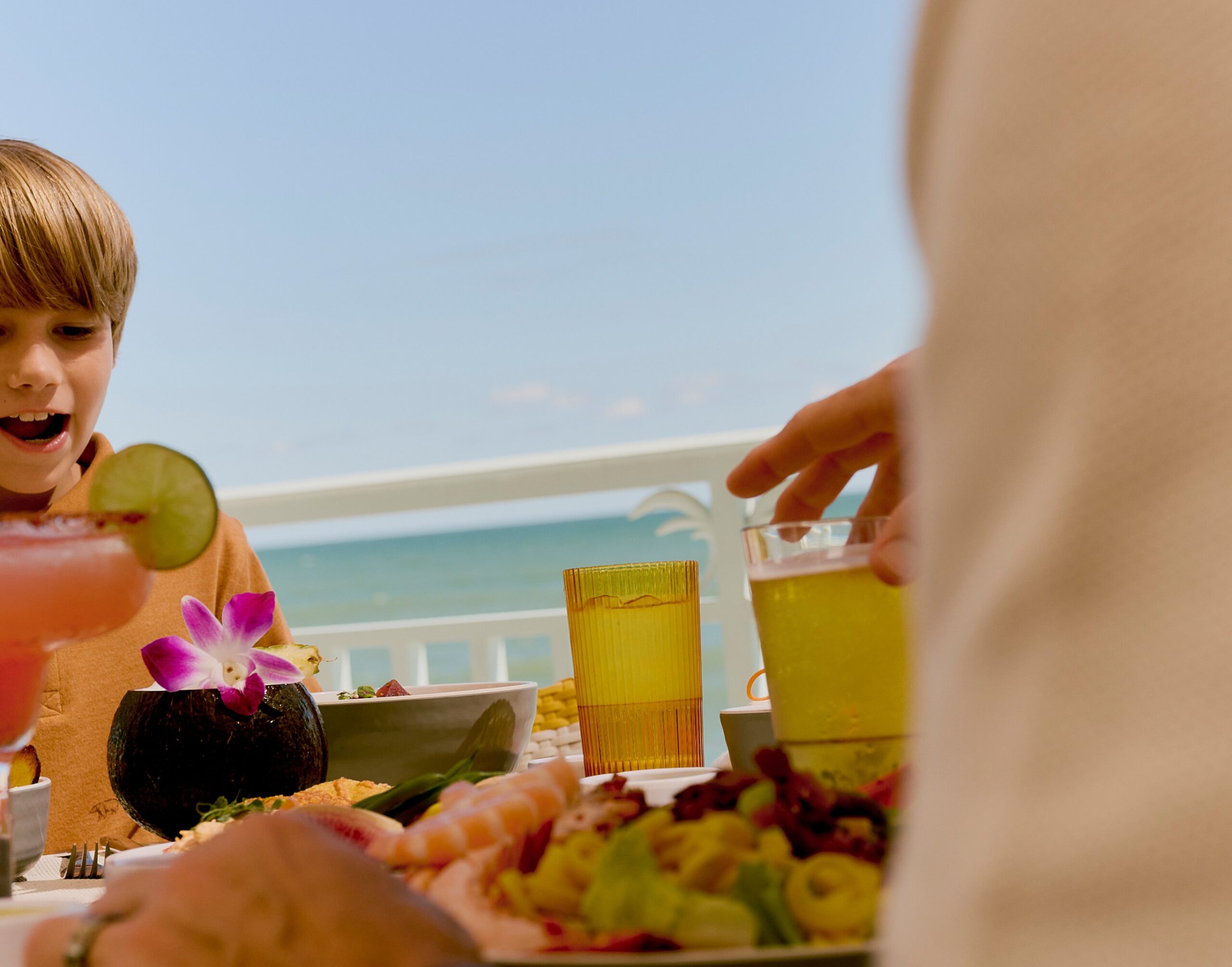 Child smiling at seaside table with tropical drinks and seafood dishes