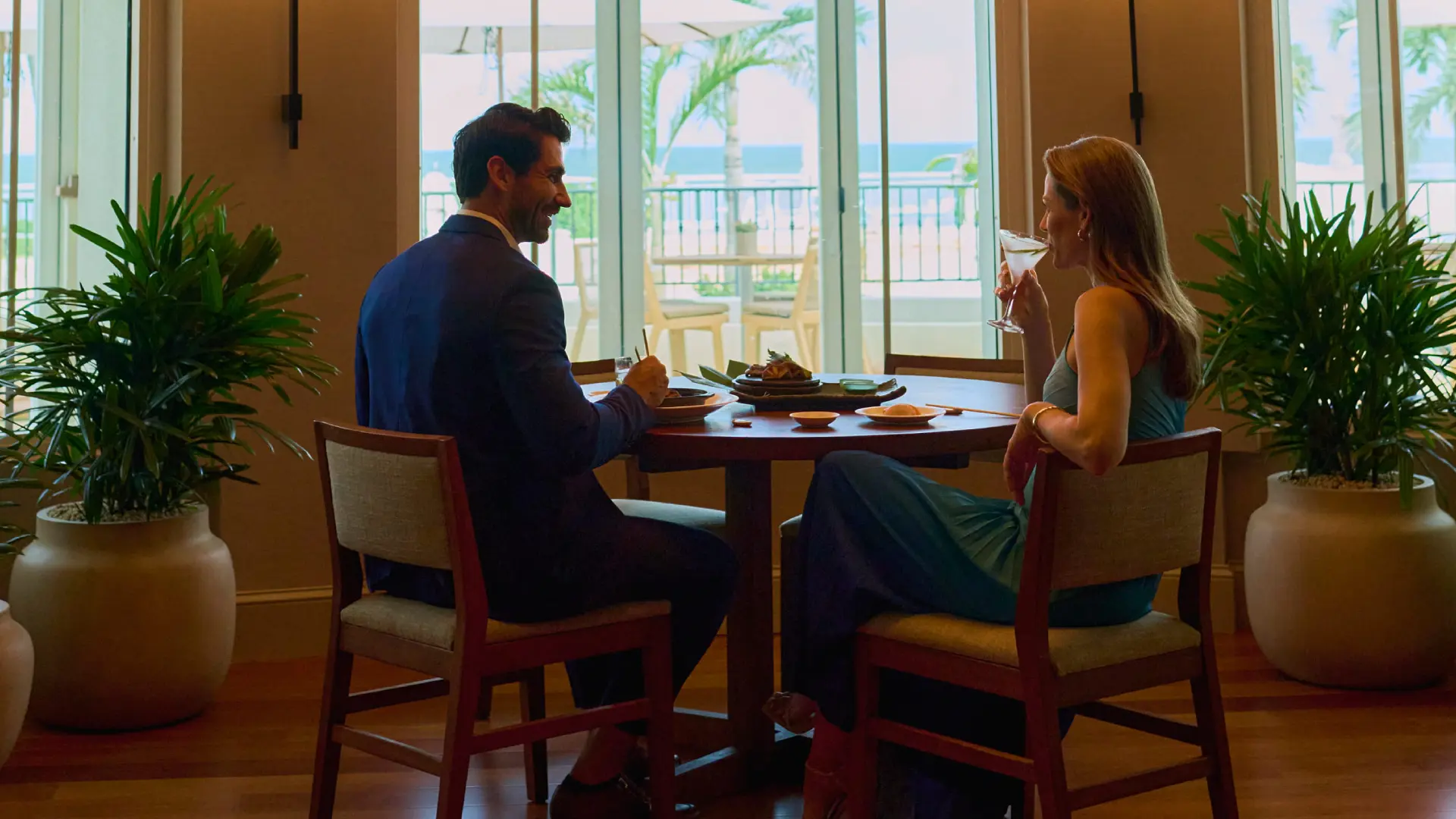 Epicurean encounter 6 Couple dining by ocean view window, enjoying drinks and meal at intimate restaurant table