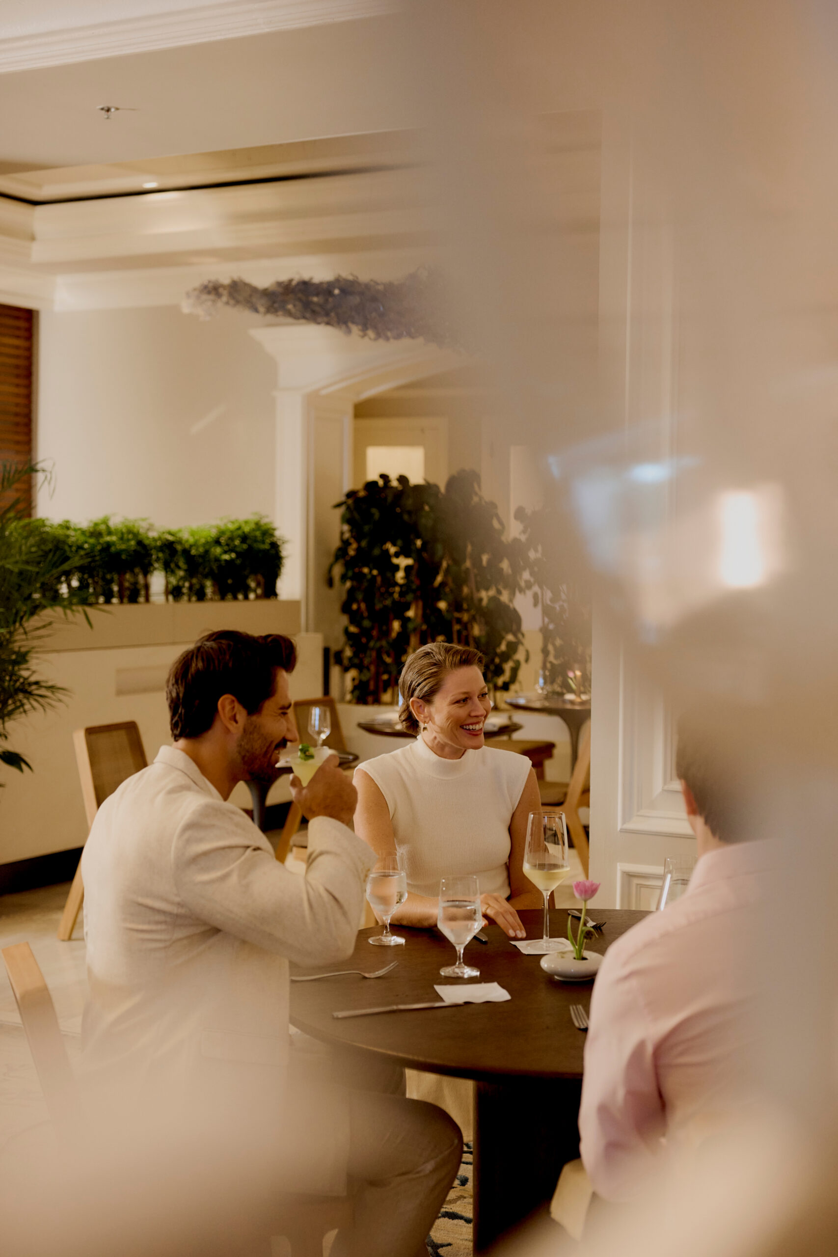 Three people enjoying drinks and conversation at elegant restaurant table indoors