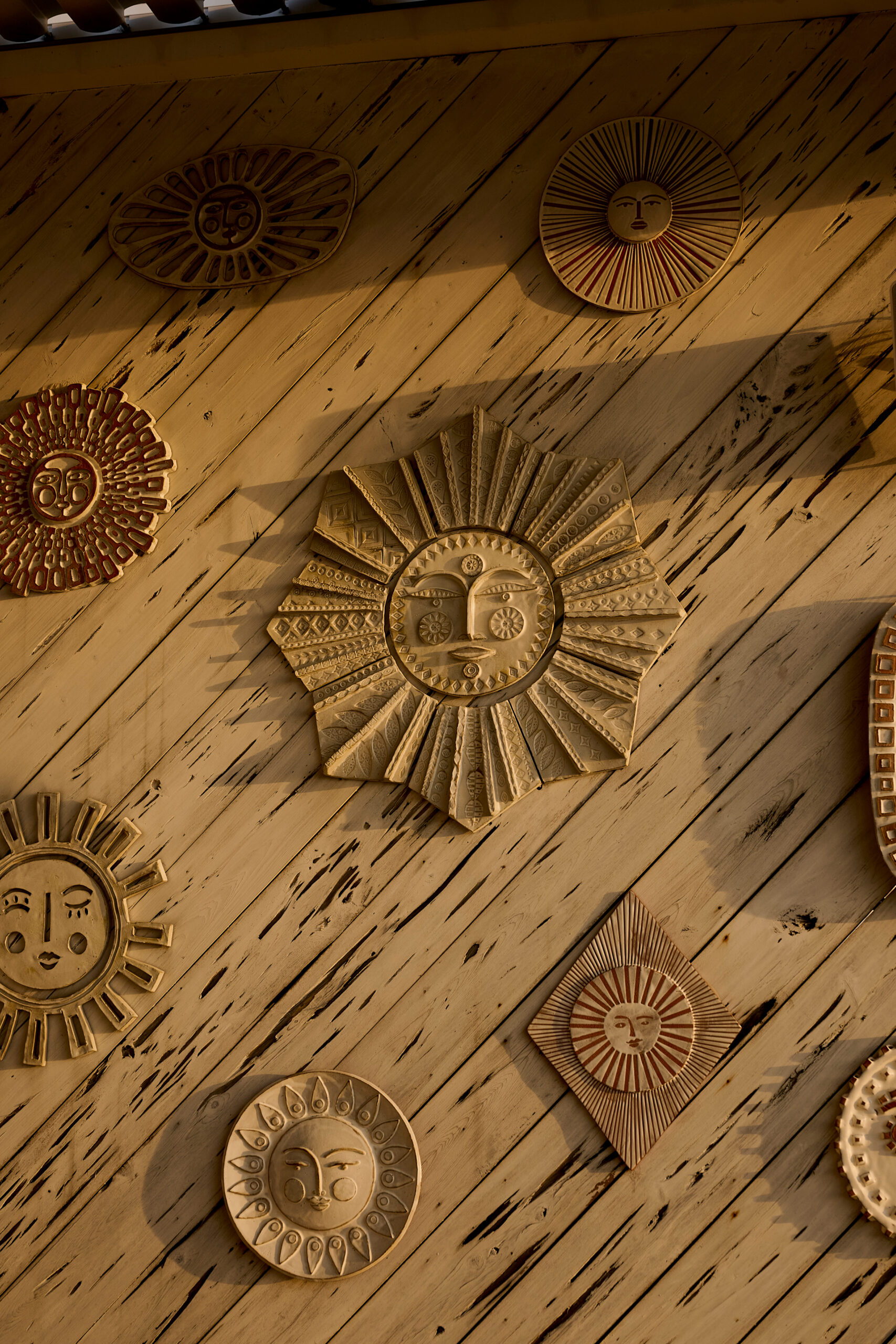 Decorative sun face wall art arranged on rustic wooden plank wall in warm light