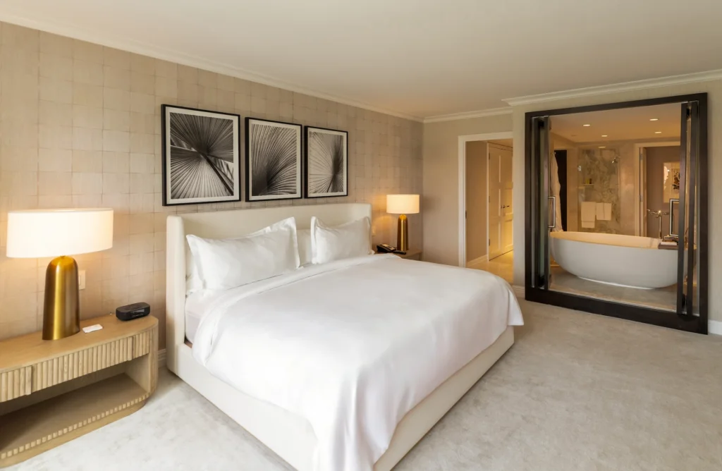 Modern bedroom suite with a plush bed, warm lighting and a glass partition revealing a marble bathroom