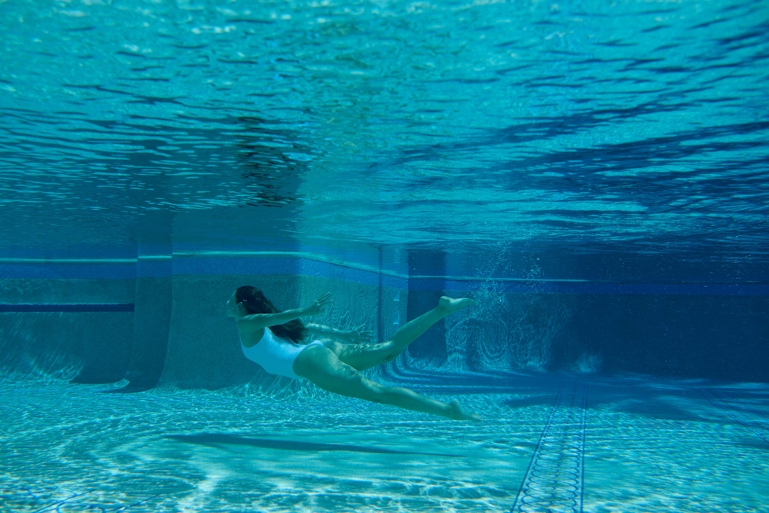 Woman swimming underwater in a pool wearing a white swimsuit