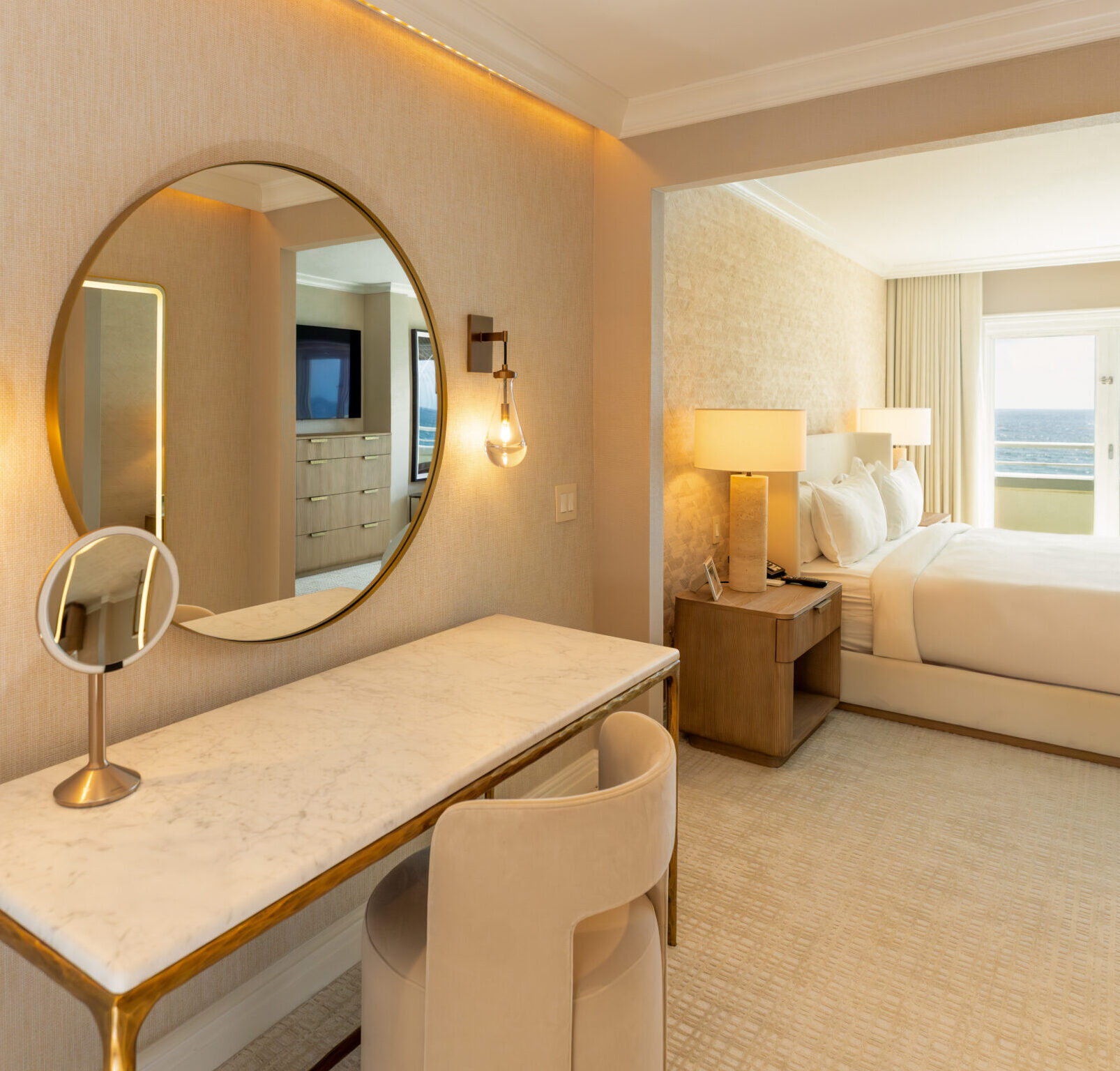 Modern hotel room with vanity desk and ocean view bedroom through balcony doors
