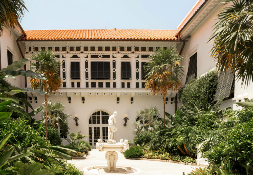 Elegant courtyard with central fountain statue, palm trees and white villa with red tiled roof