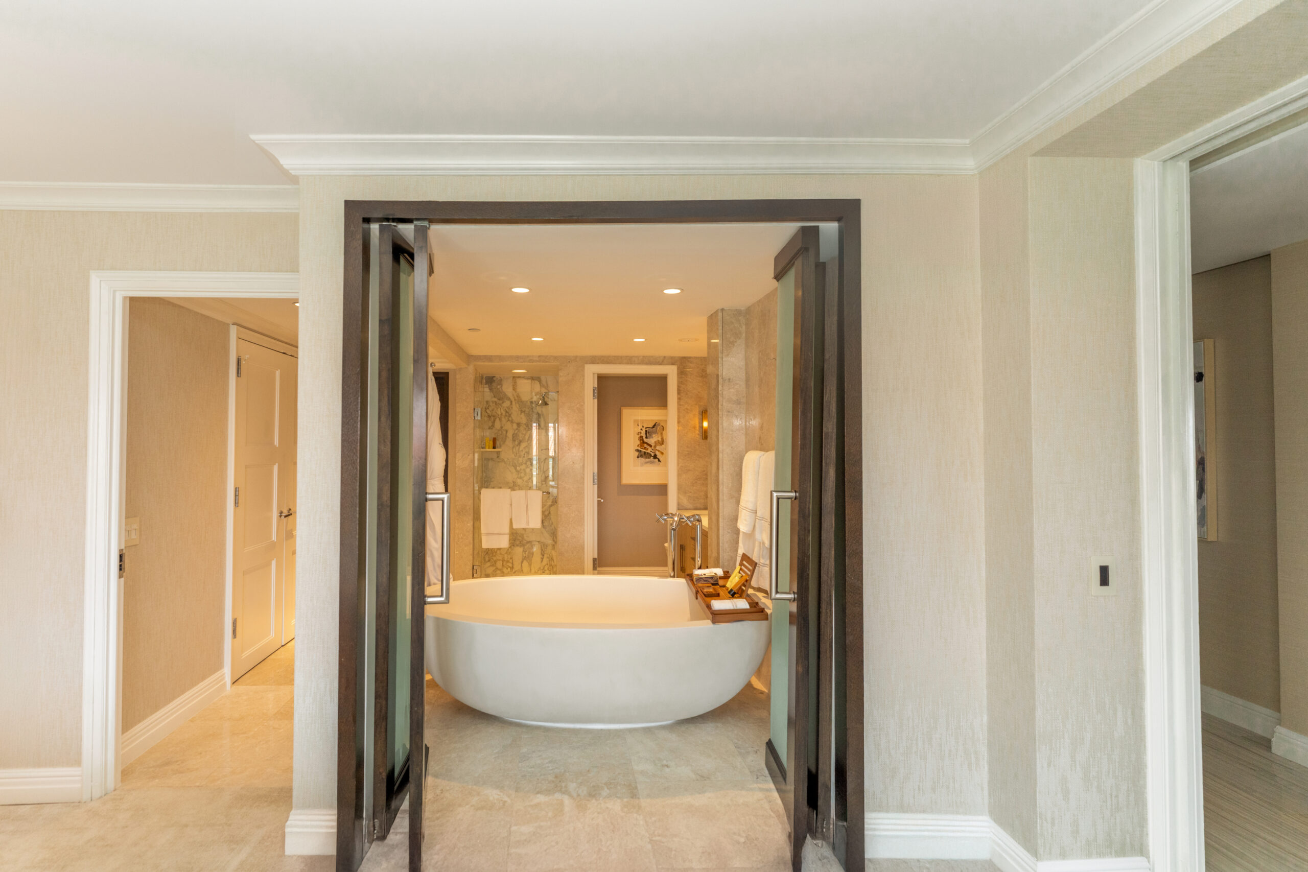 Spacious luxury bathroom with freestanding bathtub, marble walls, and open double doors