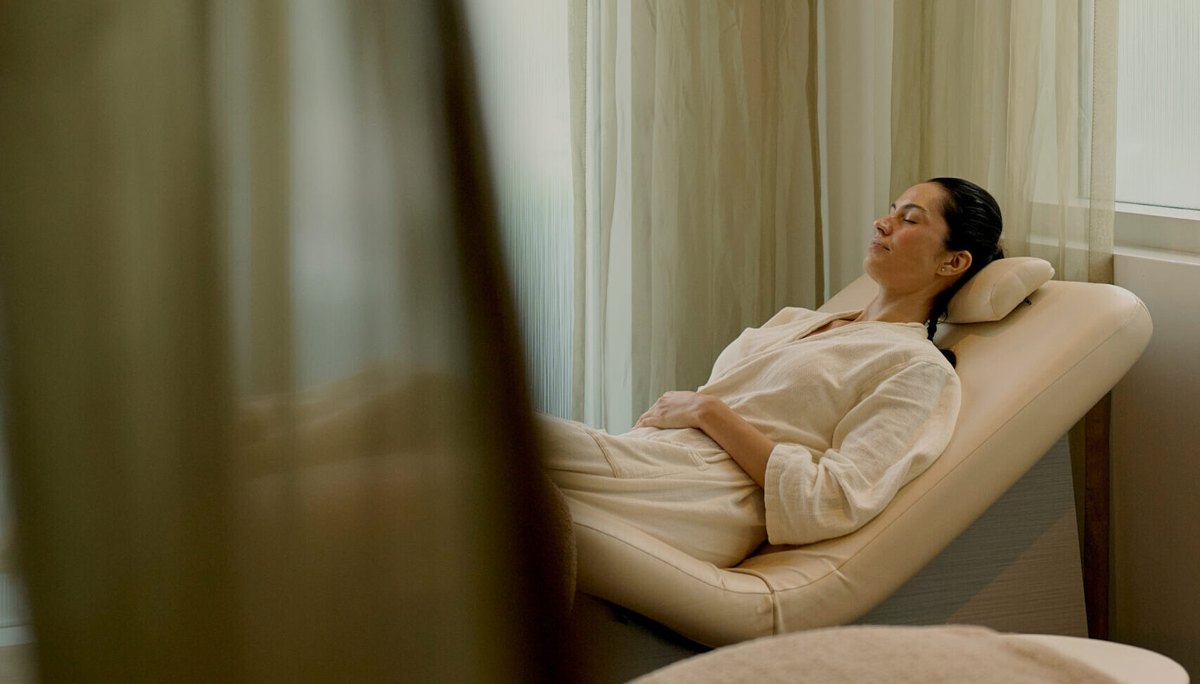 Woman lying relaxed on spa recliner with eyes closed in softly lit wellness room