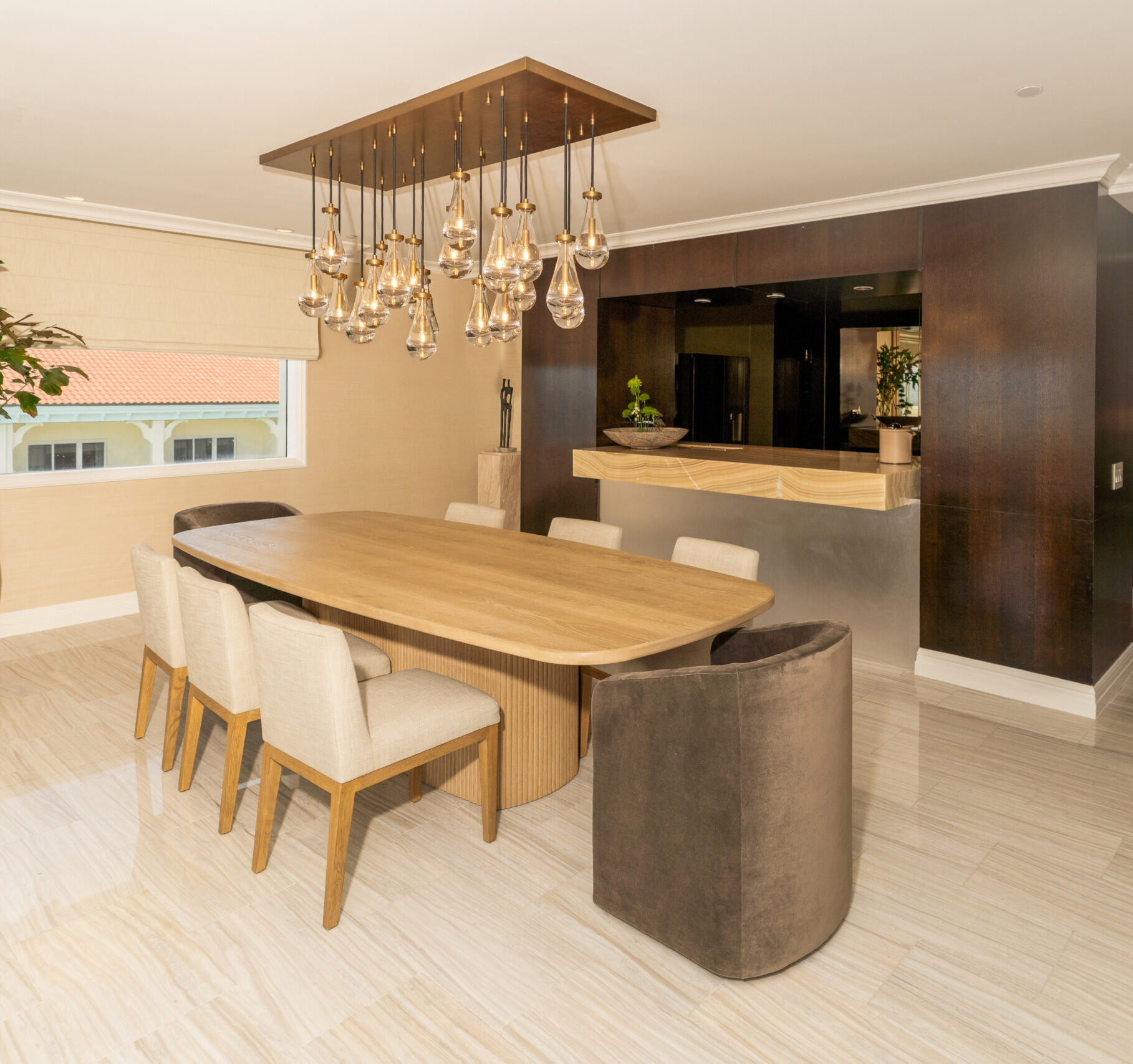 Modern dining room with wooden table, upholstered chairs, and pendant lights beside dark wood kitchen area