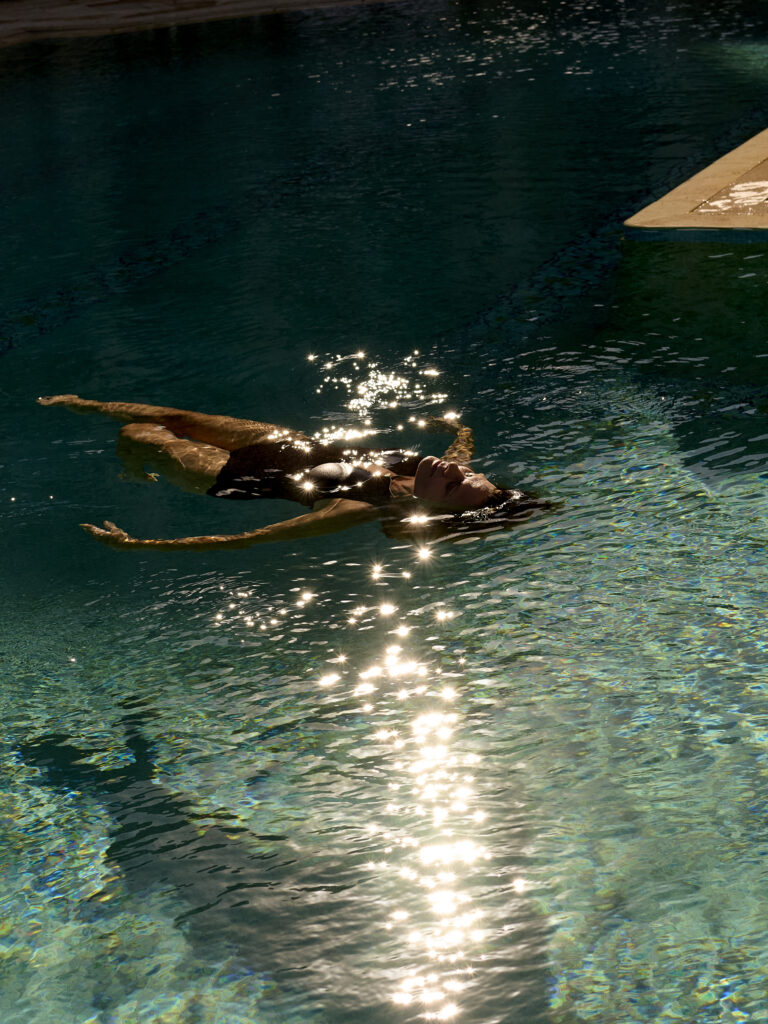 Woman floating on her back in sunlit pool with sparkling reflections on clear blue water