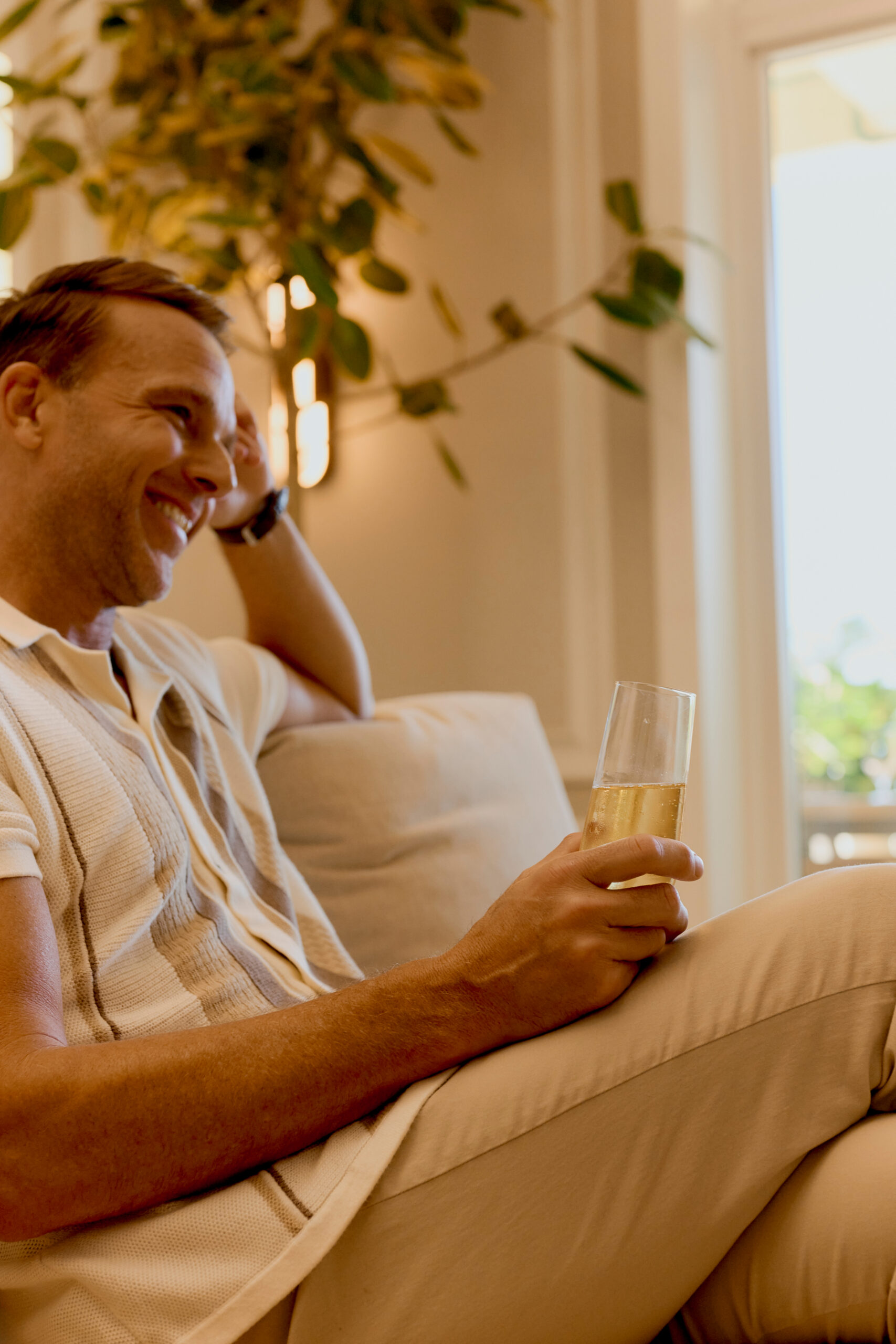 Smiling man relaxing on a sofa holding a glass of champagne in a bright living room