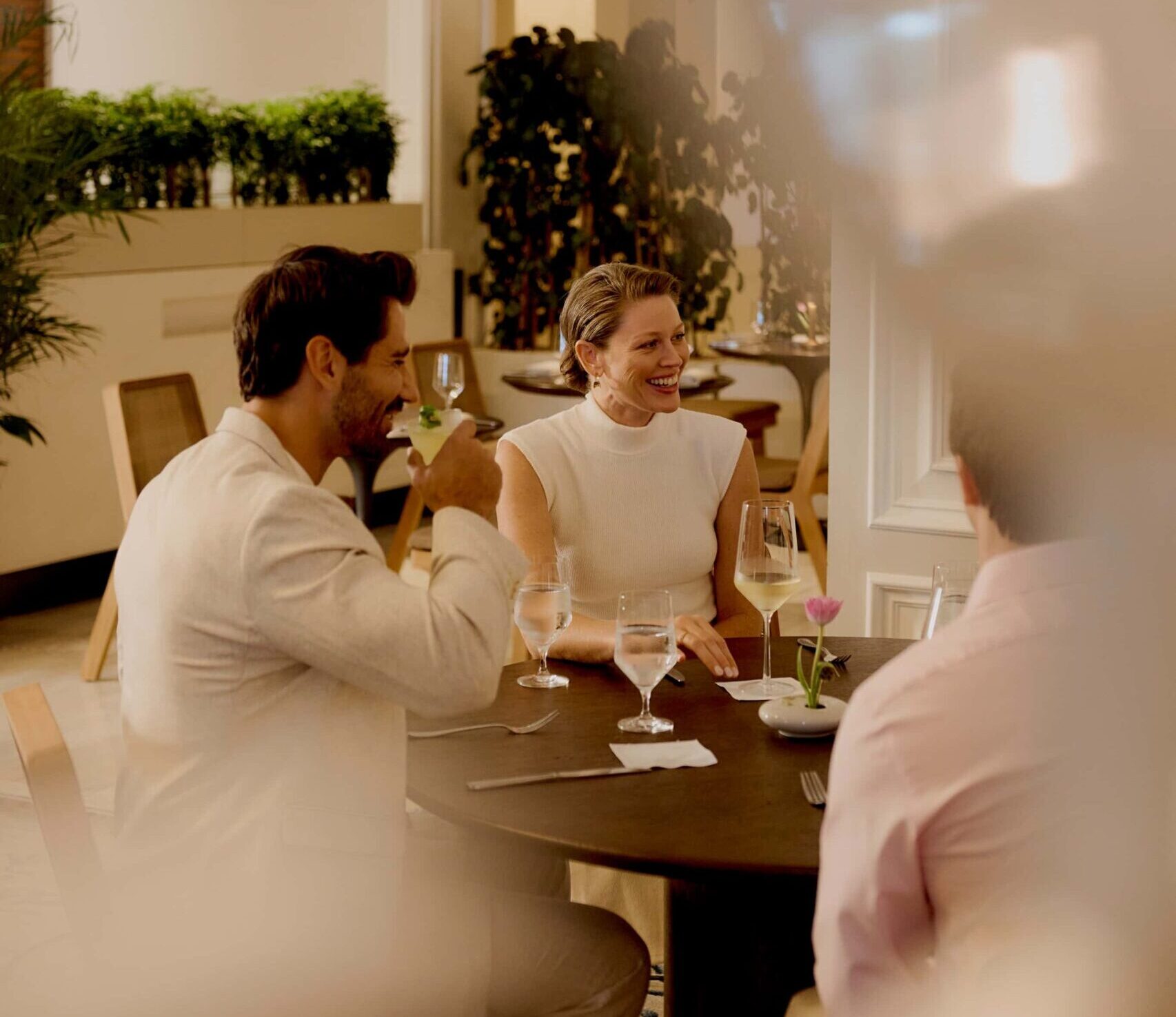 Three adults enjoying drinks and conversation at a restaurant table in a bright, modern dining room