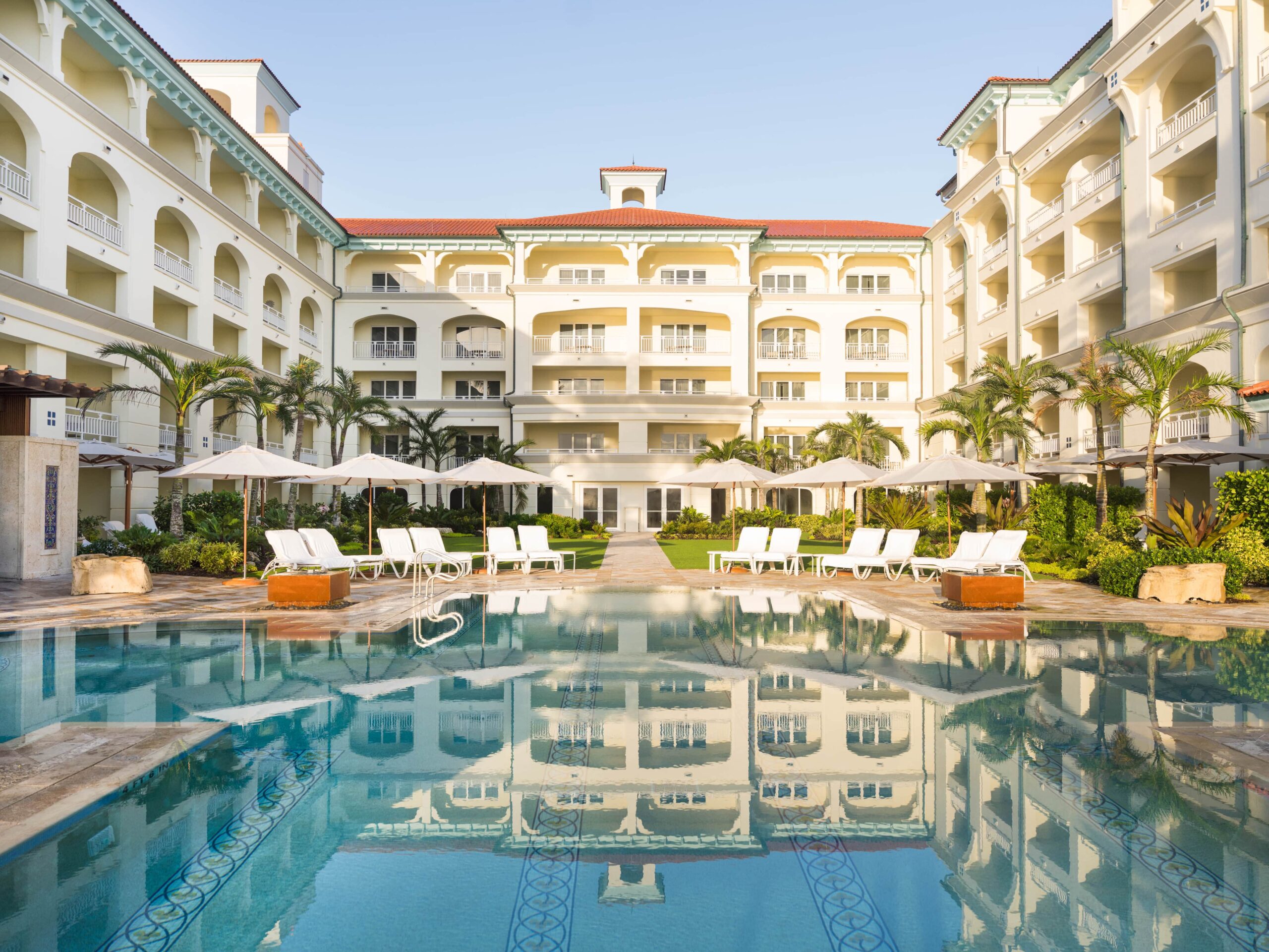 Luxury resort courtyard with palm trees, pool, and sun loungers under clear sky