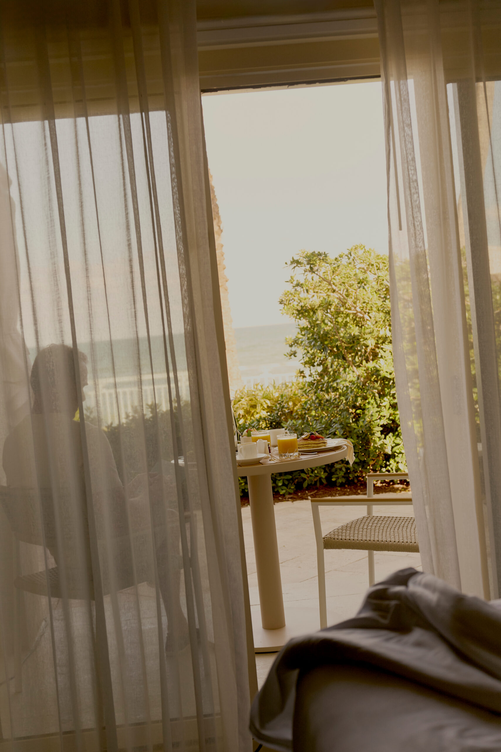 Breakfast table on sunlit balcony with ocean view seen through sheer curtains
