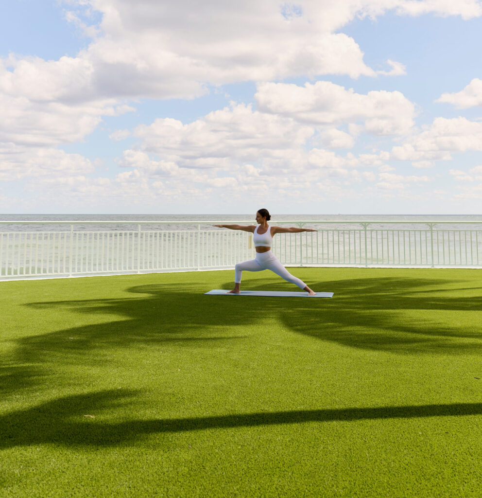 Woman practicing yoga on lawn overlooking ocean under blue sky with clouds