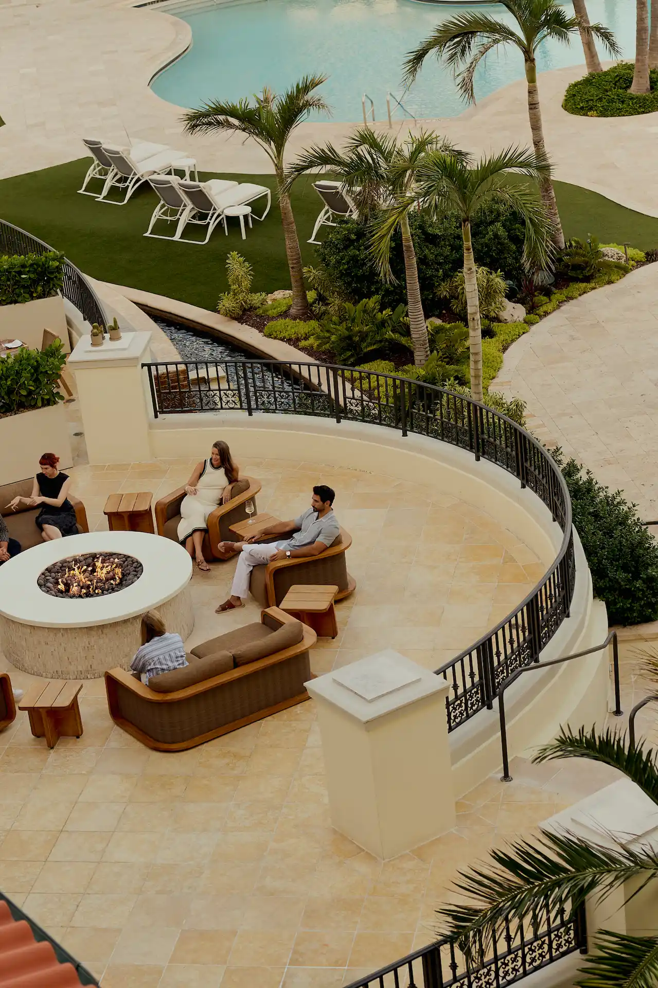 People gathered around a glowing fire pit in a lush poolside lounge at eau palm beach