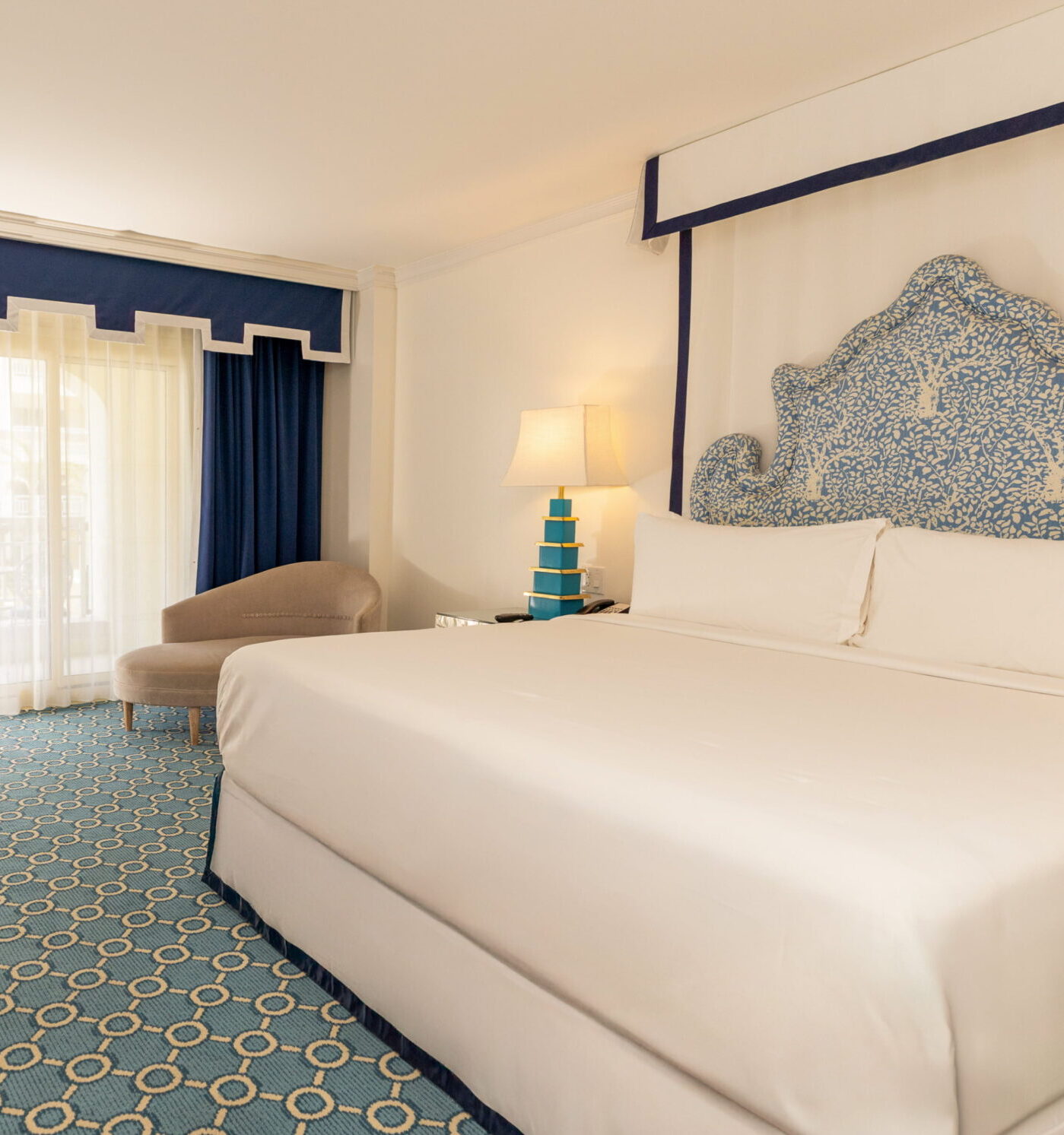 Bright coastal hotel room with king bed, blue accents, and balcony doors