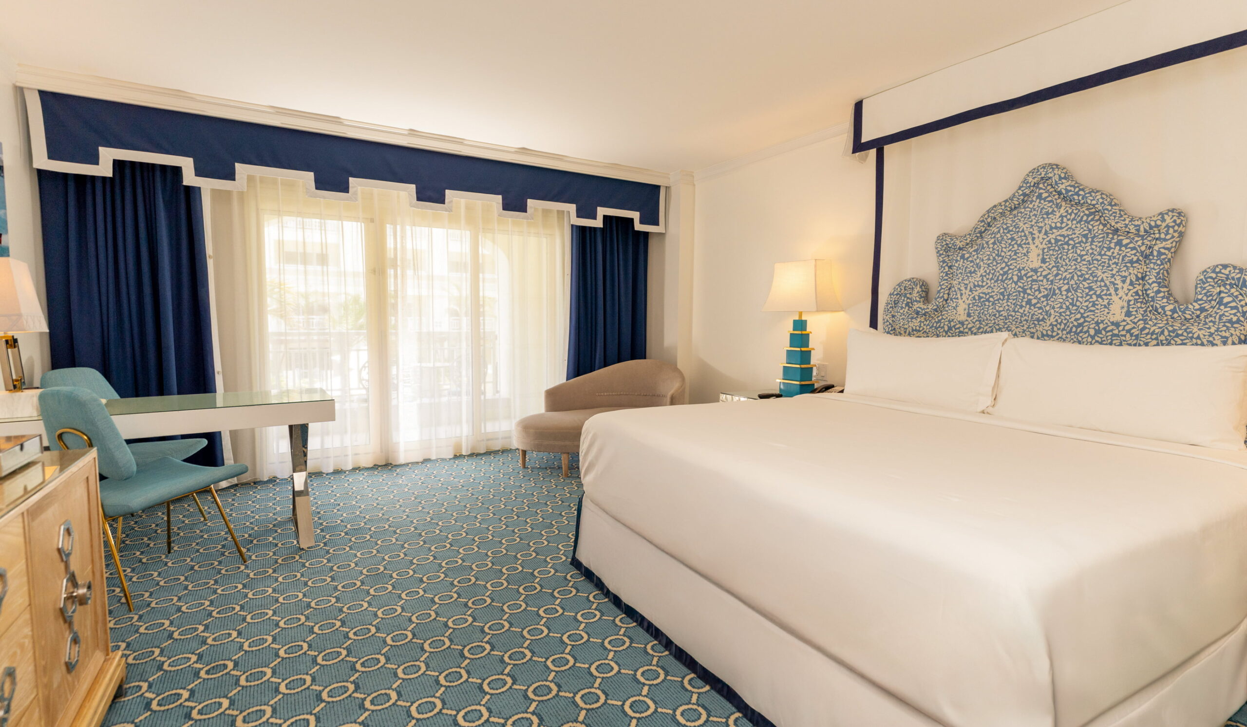 Bright coastal hotel room with king bed, blue accents, and balcony doors