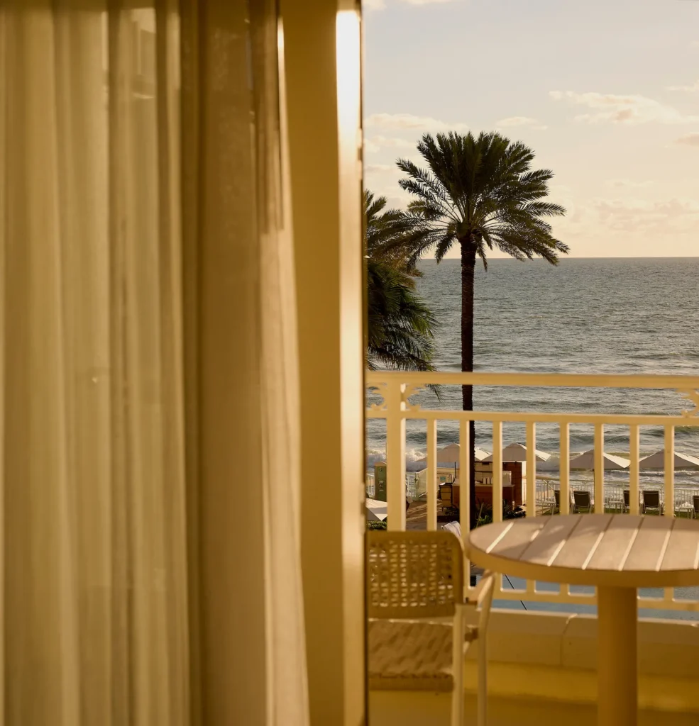 Balcony view with a chair and table overlooking palm trees, beach umbrellas and a calm ocean