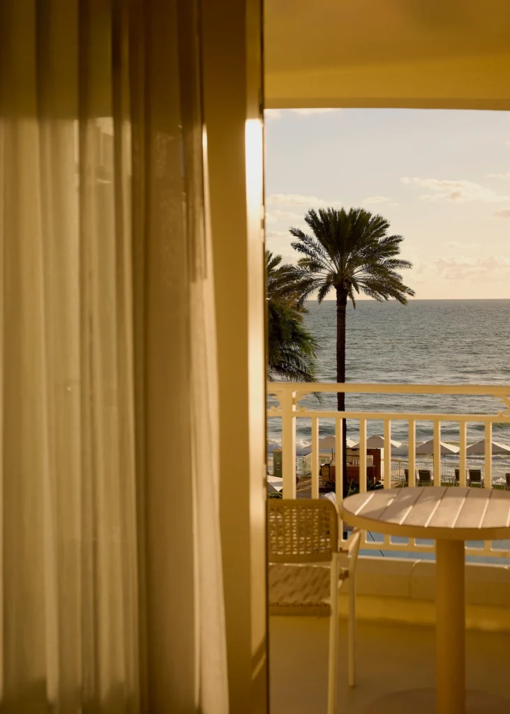 Balcony view with a chair and table overlooking palm trees, beach umbrellas and a calm ocean