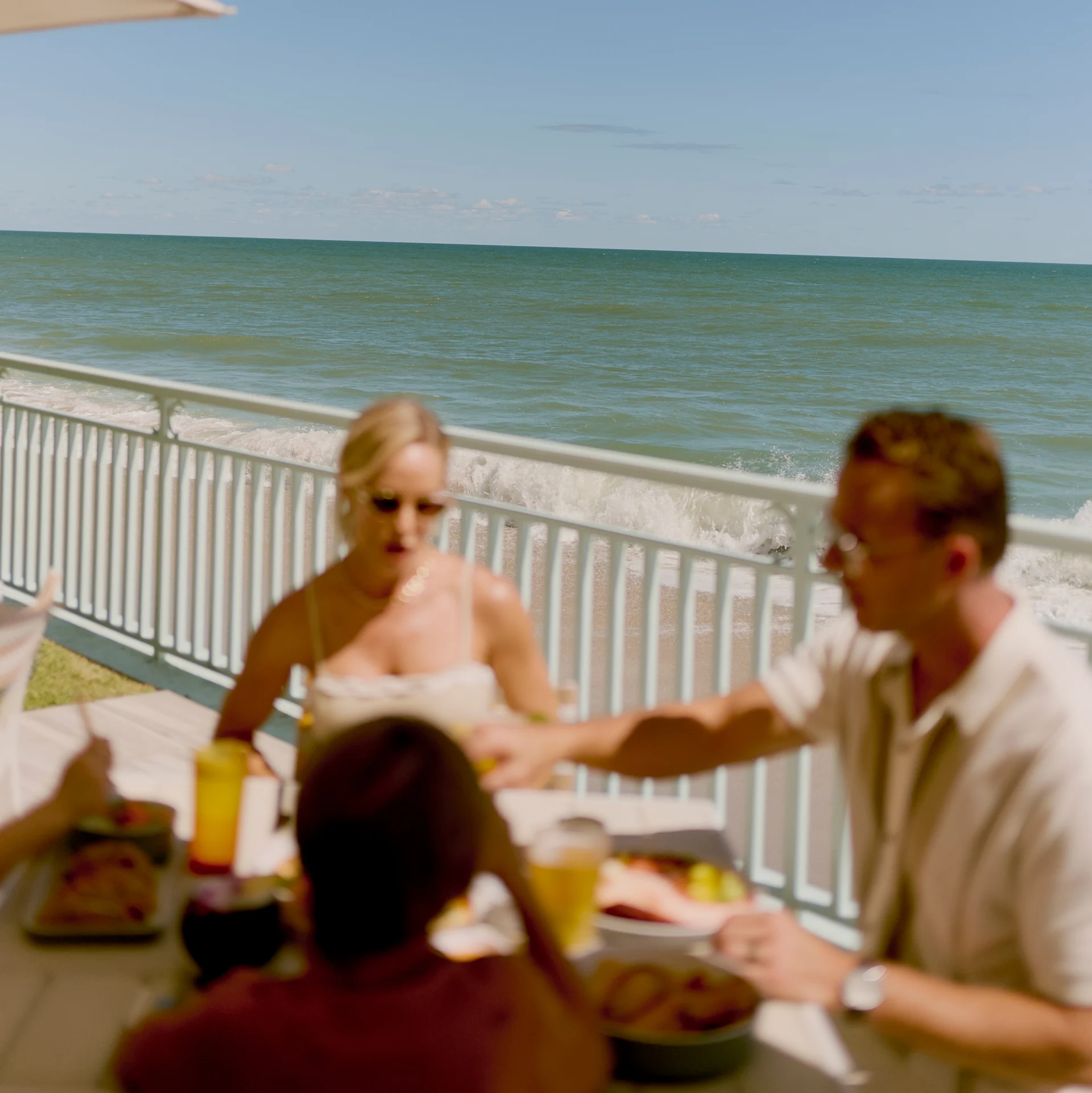 Guests enjoy an oceanfront meal with waves and soft sunlight creating a relaxed coastal atmosphere