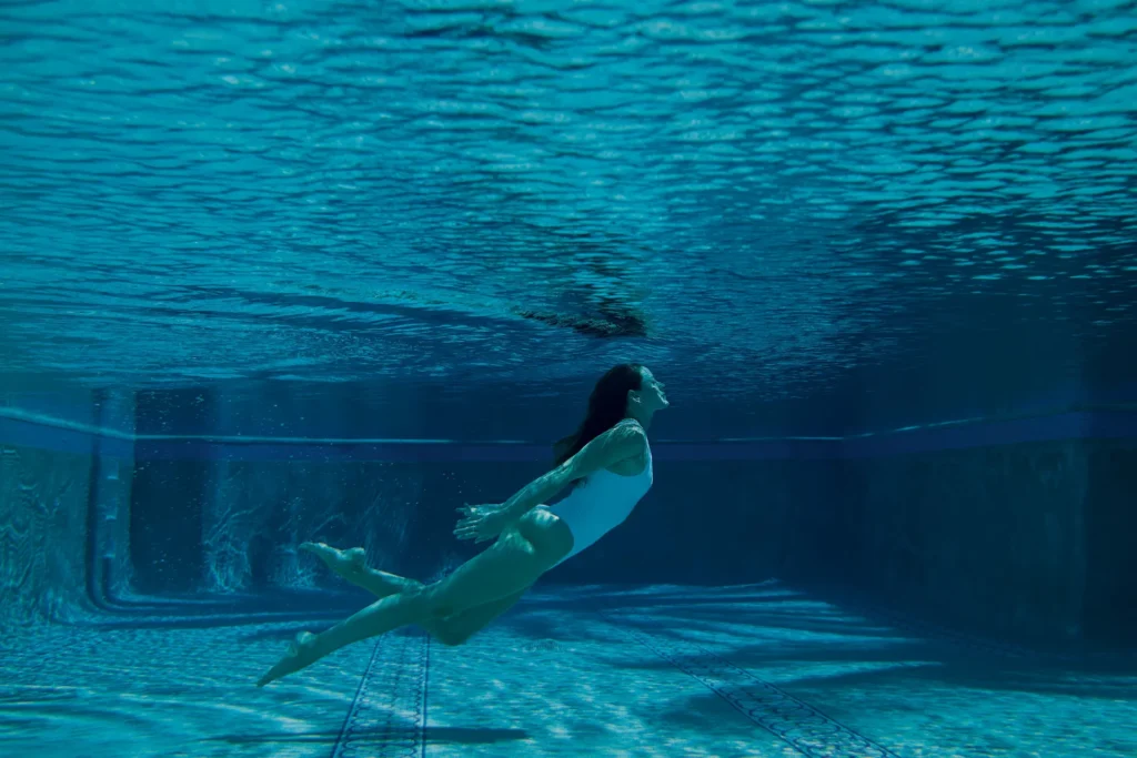 Underwater swimmer gliding forward in a white suit, surrounded by clear blue water and rippling reflections