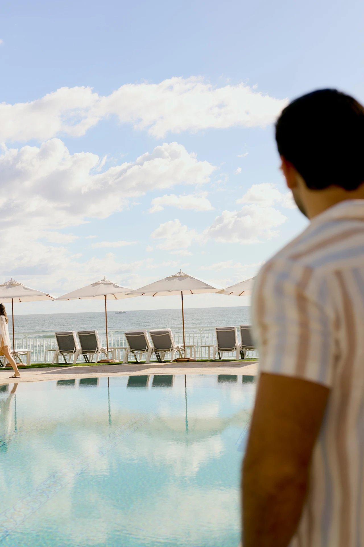 Peaceful poolside scene with white umbrellas, palm trees and ocean views creating a calm coastal escape